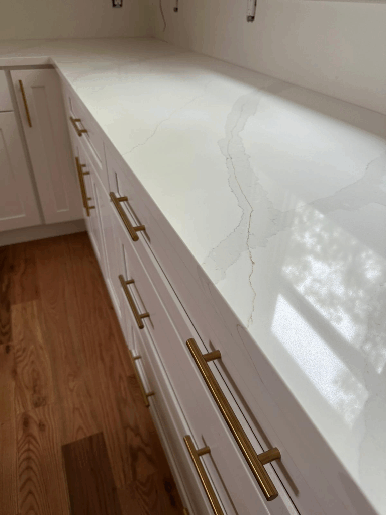 White countertop with brass handles and wood floor in a bright kitchen.