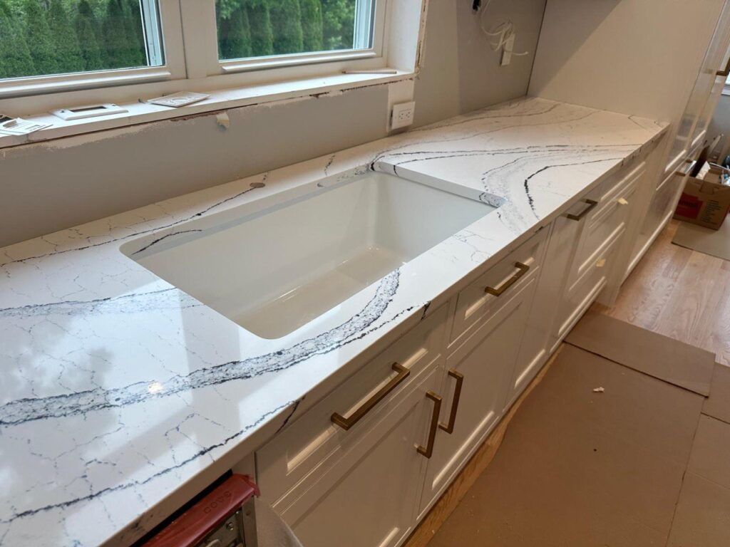 White bathroom vanity with marble countertop, built-in sink, and drawers below a window.