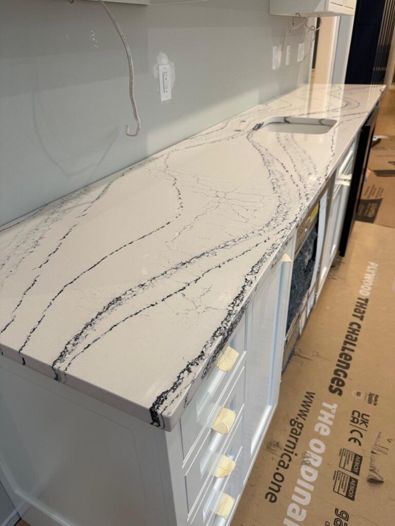 Marble-look kitchen countertop with gray veining beside white cabinets and a stainless appliance