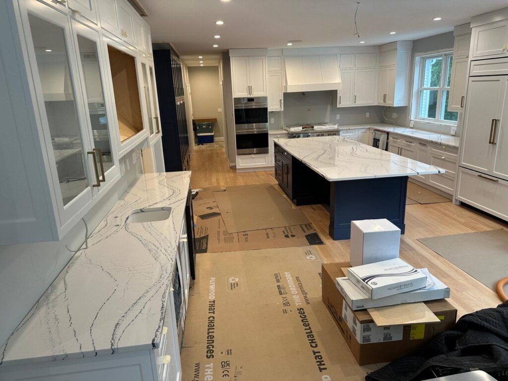 Modern kitchen under renovation with white cabinets, marble island, and cardboard floor protection