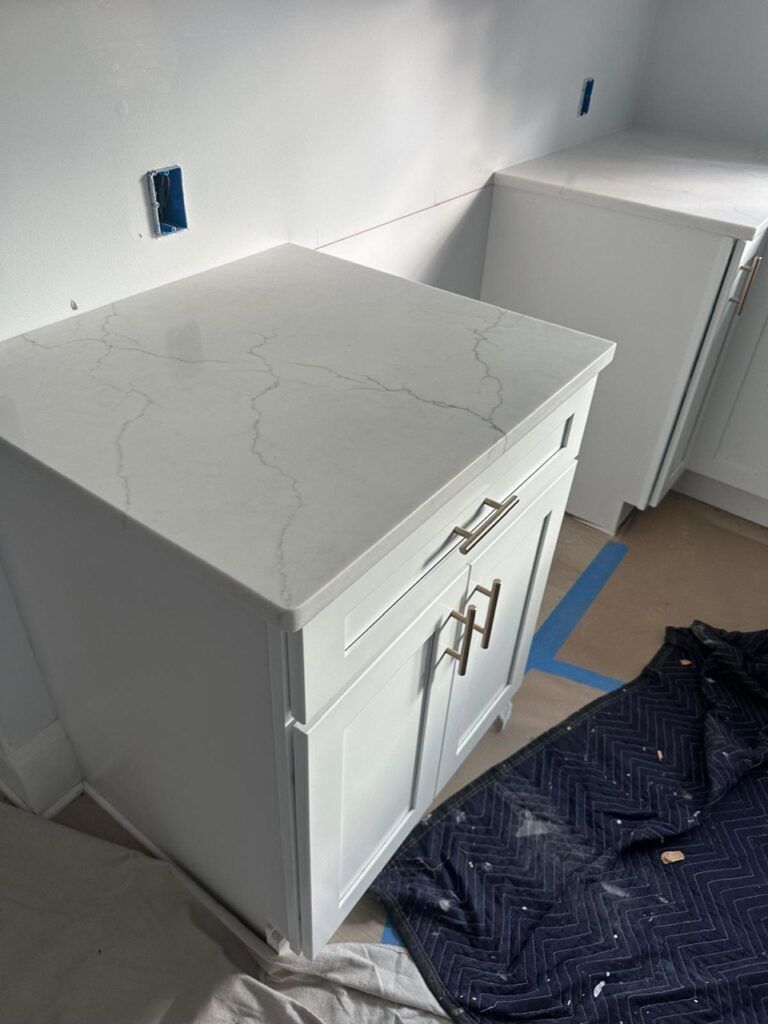 White cabinet with marble-look top in an unfinished room, surrounded by taped walls and floor protection.