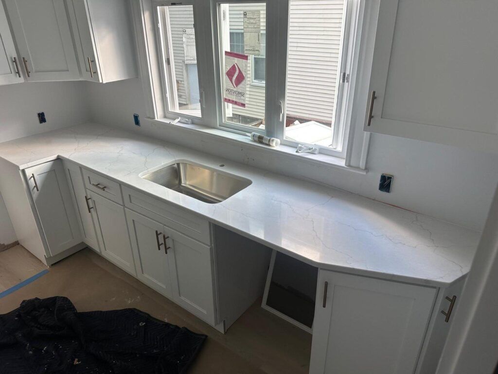 Kitchen countertop with sink, white cabinets, and a window above the sink under renovation.