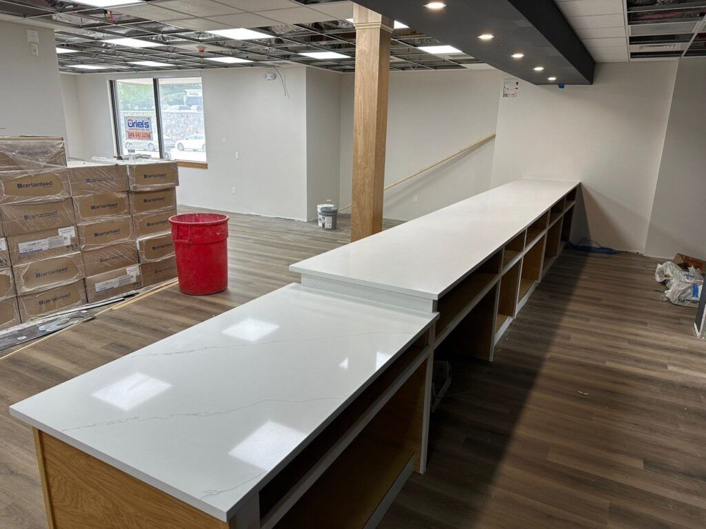 Long white retail counter in an unfinished store with stacked boxes, red bin, and exposed ceiling bulbs