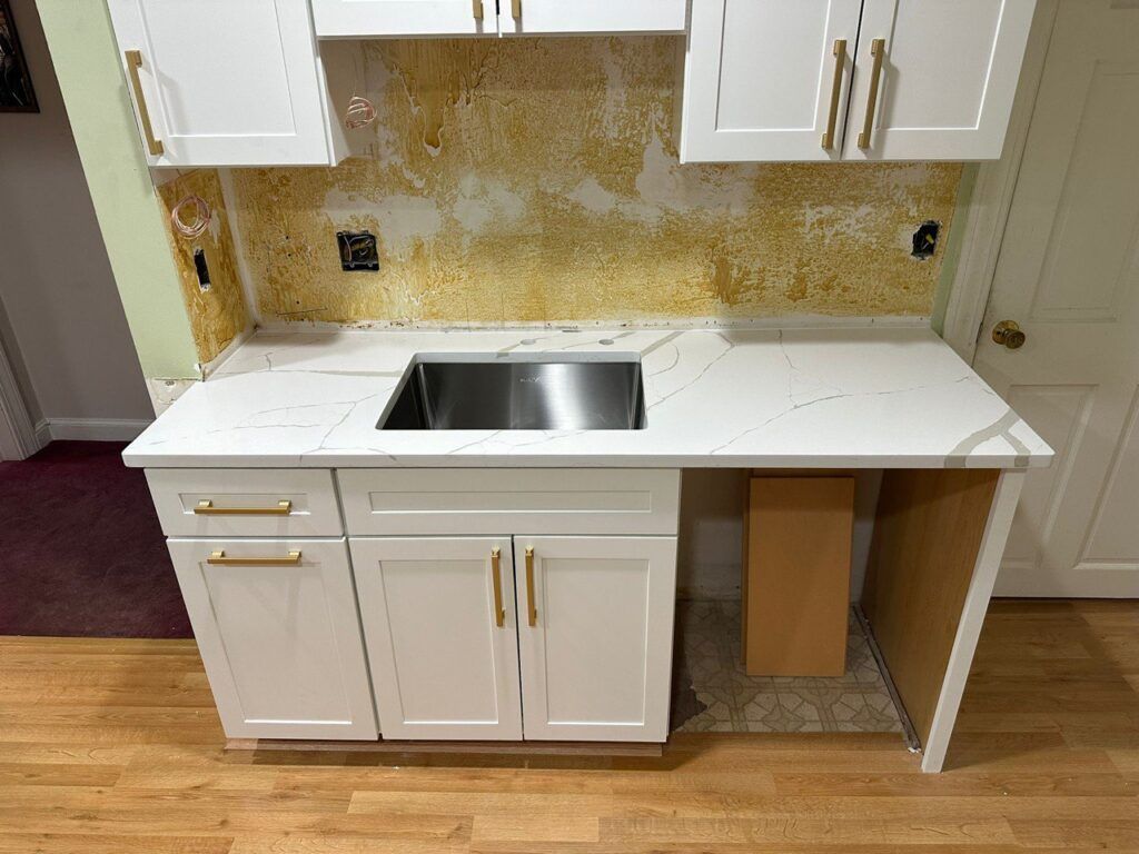 Small kitchen with white cabinets, marble countertop, double sink, and unfinished backsplash area.