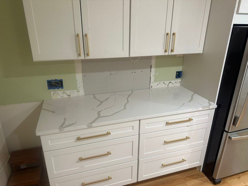 White kitchen cabinets with gold handles and a marble-pattern countertop beside a black refrigerator.
