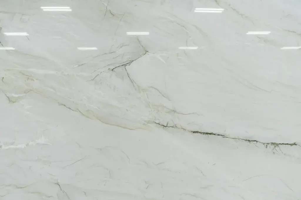 White marble-like tiled wall with gray veining and bright reflections from overhead lights