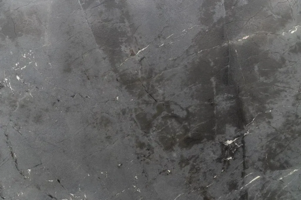 Close-up of a gray, cracked stone surface with dark stains and small debris