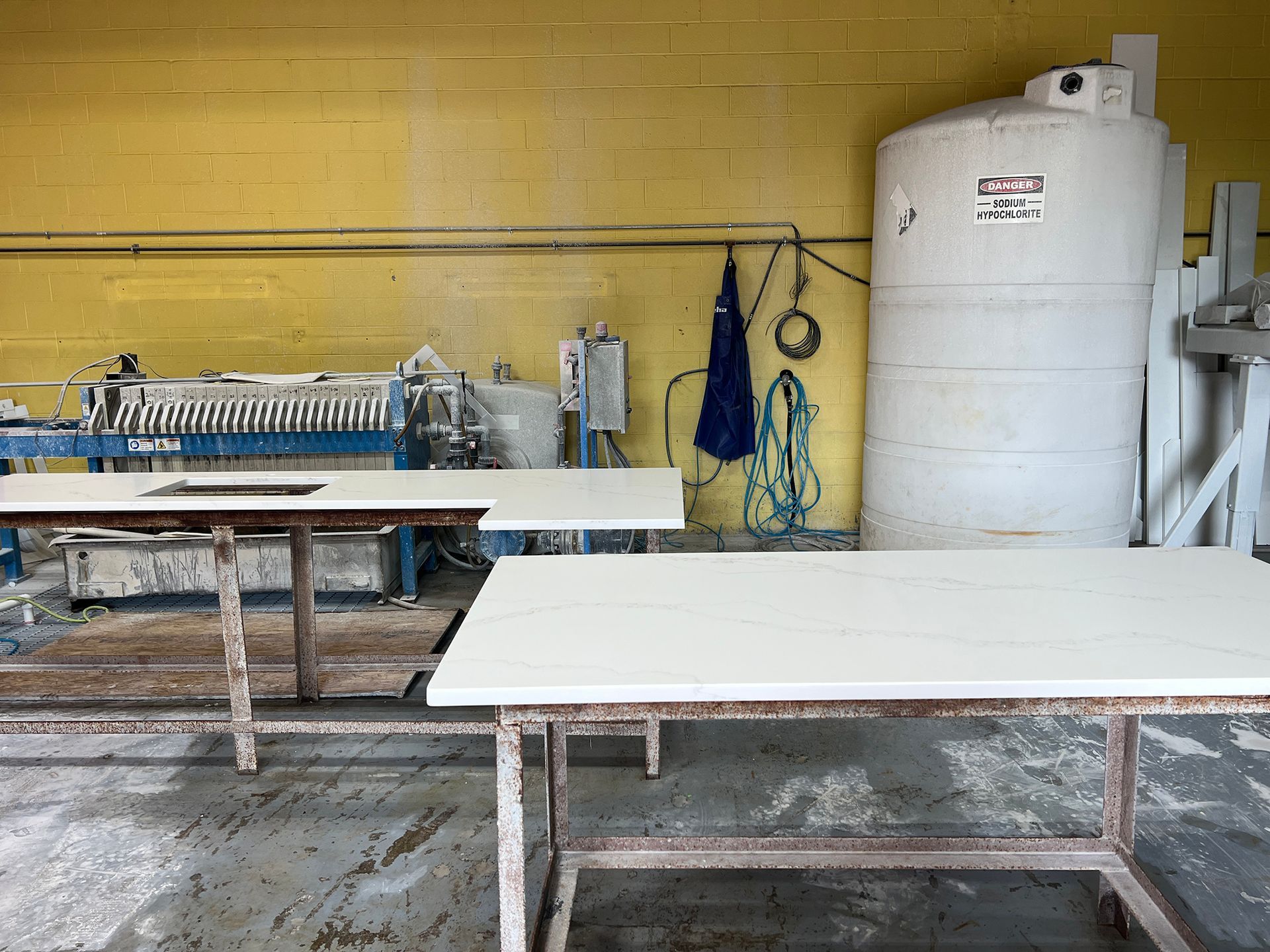 Workshop with two worktables, a large white tank, and industrial equipment against a yellow wall.