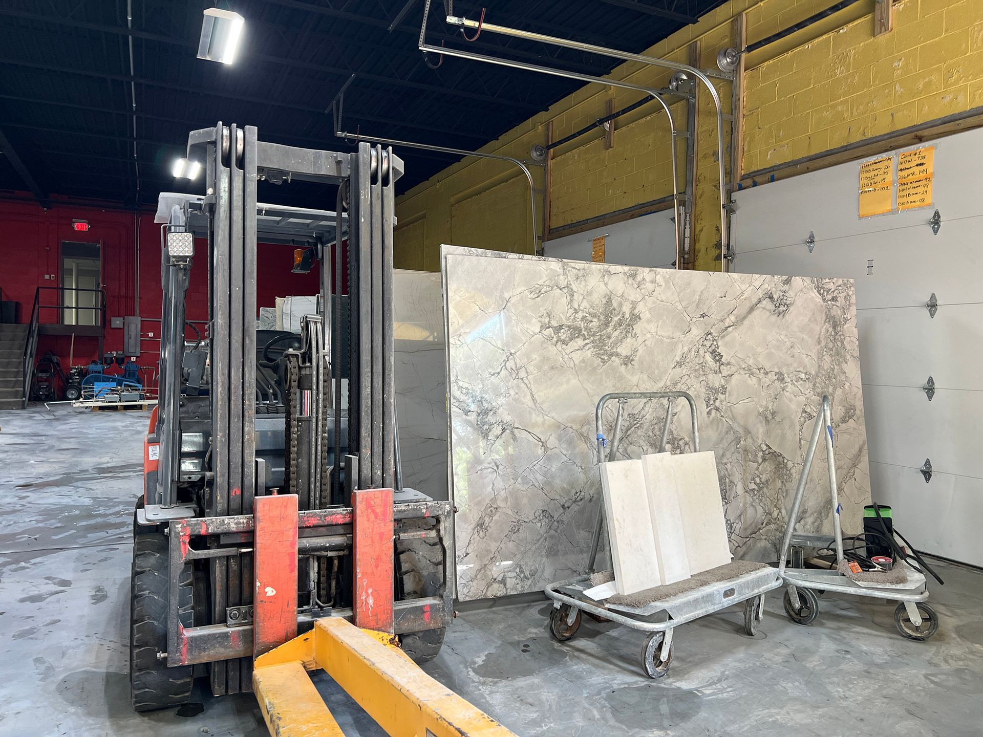 Forklift parked in an industrial warehouse beside stacked metal sheets and carts.