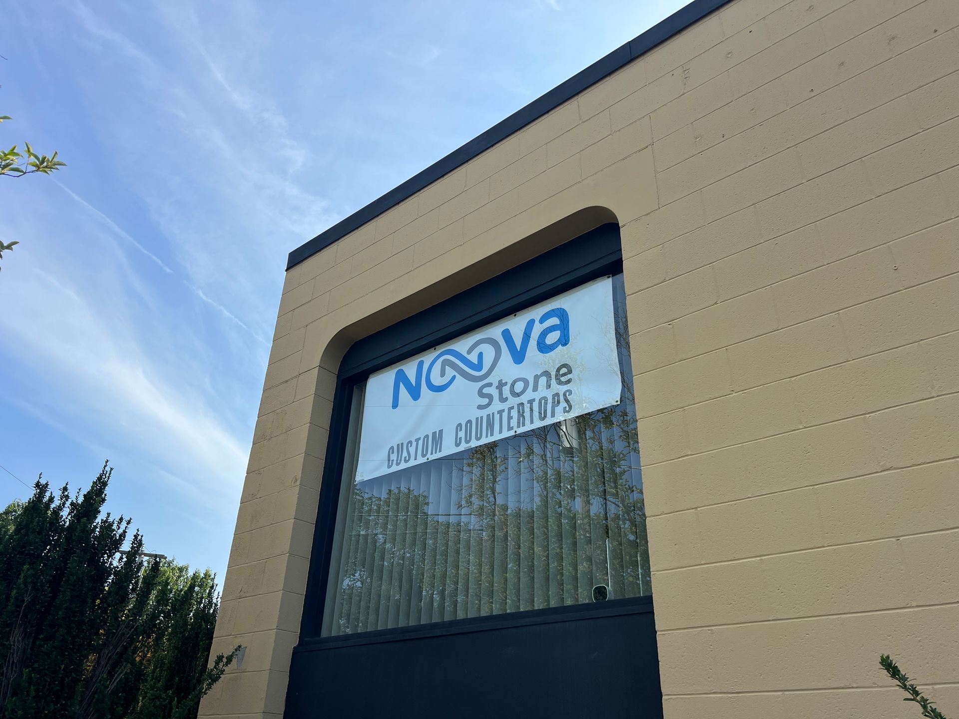 Exterior of Nova Stone storefront with blue sign on a beige building under a clear sky