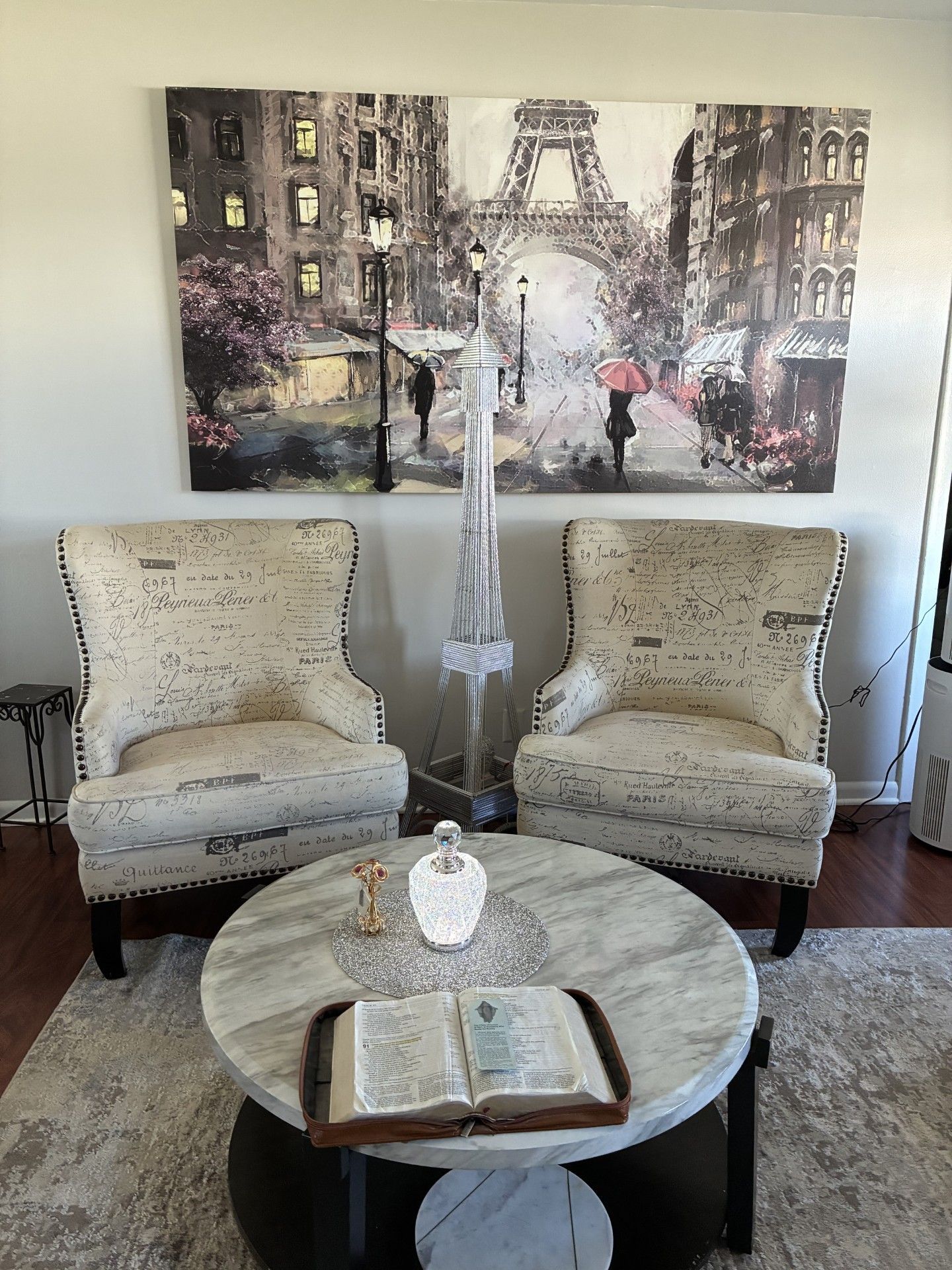 Cozy sitting area with two armchairs, round coffee table, and Eiffel Tower wall art.