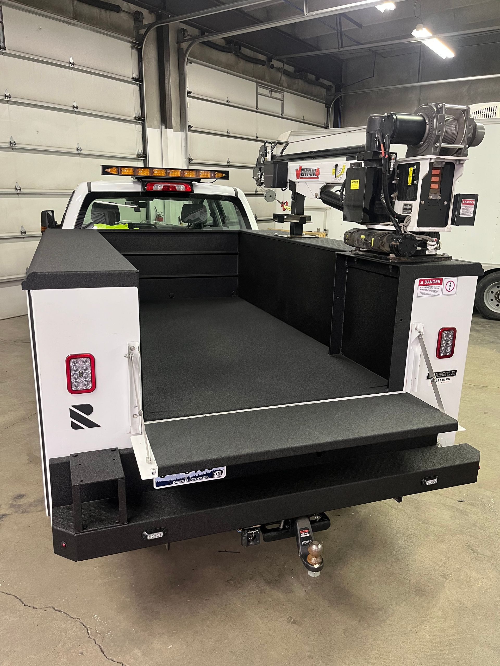 White utility truck with a rear lift bed inside a garage or workshop