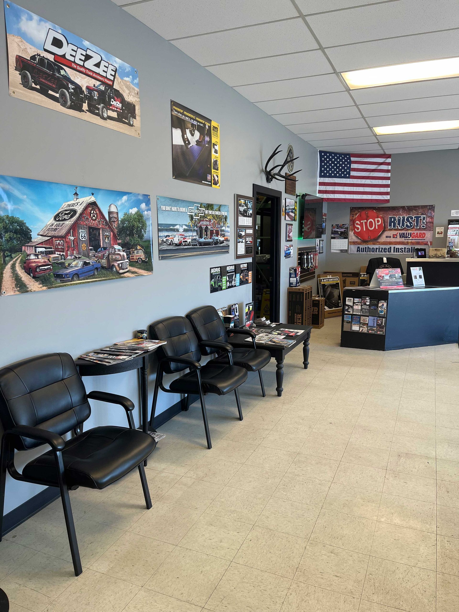 A waiting area in an office with black chairs arranged along a gray wall adorned with automotive-themed posters.