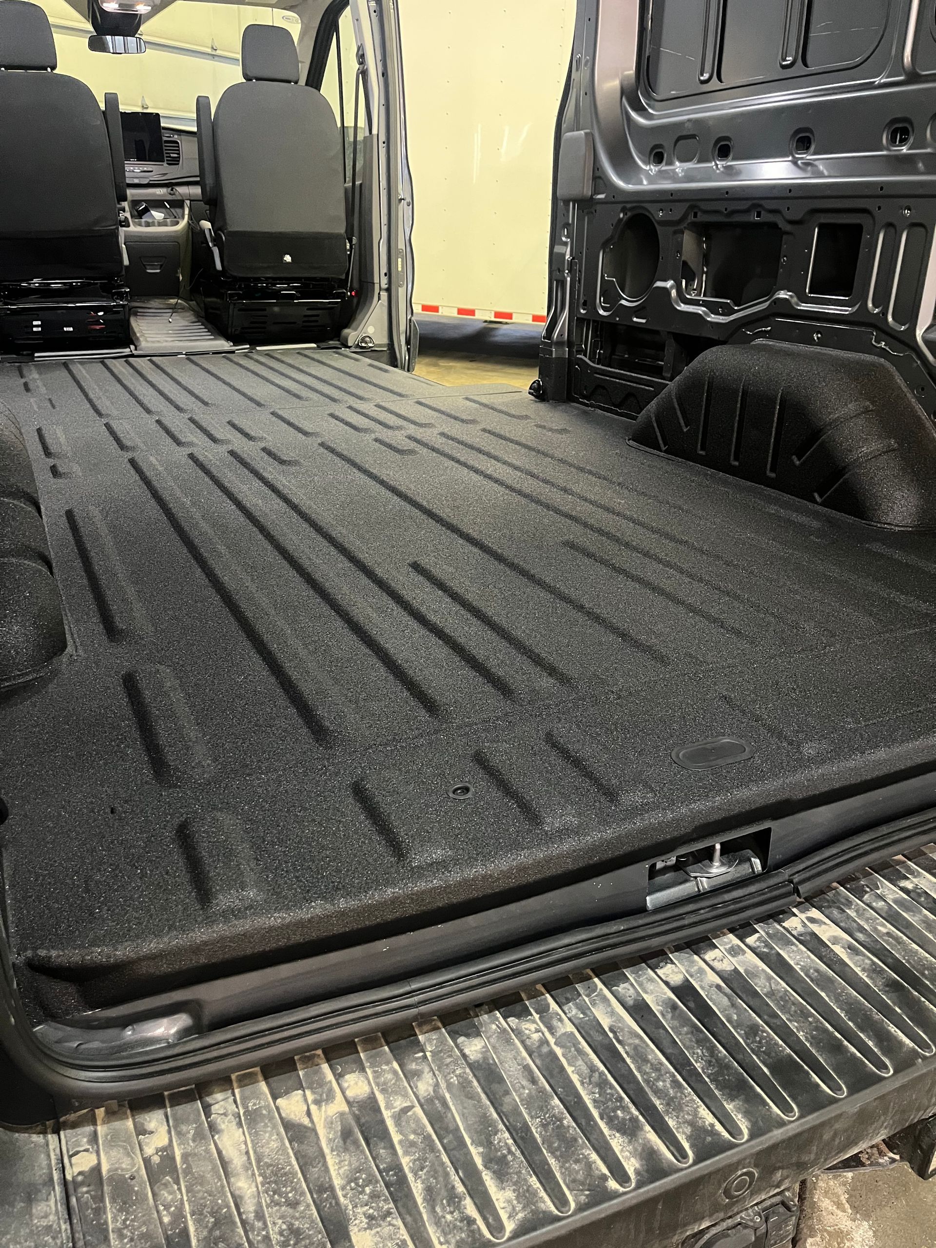 Black cargo mat and rear seat area inside a vehicle with the tailgate open.