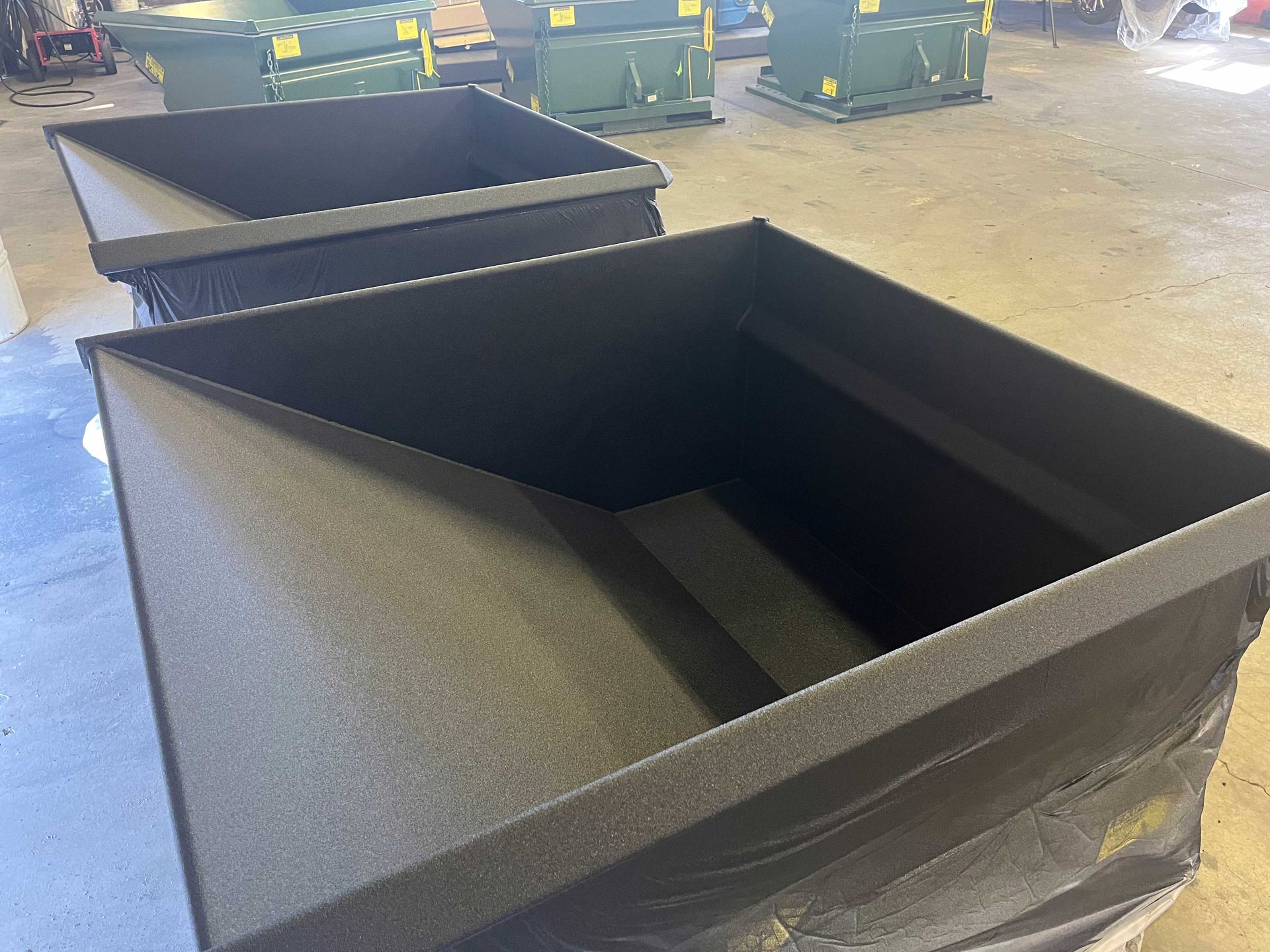 Two stacked black plastic industrial hopper bins in a warehouse setting.