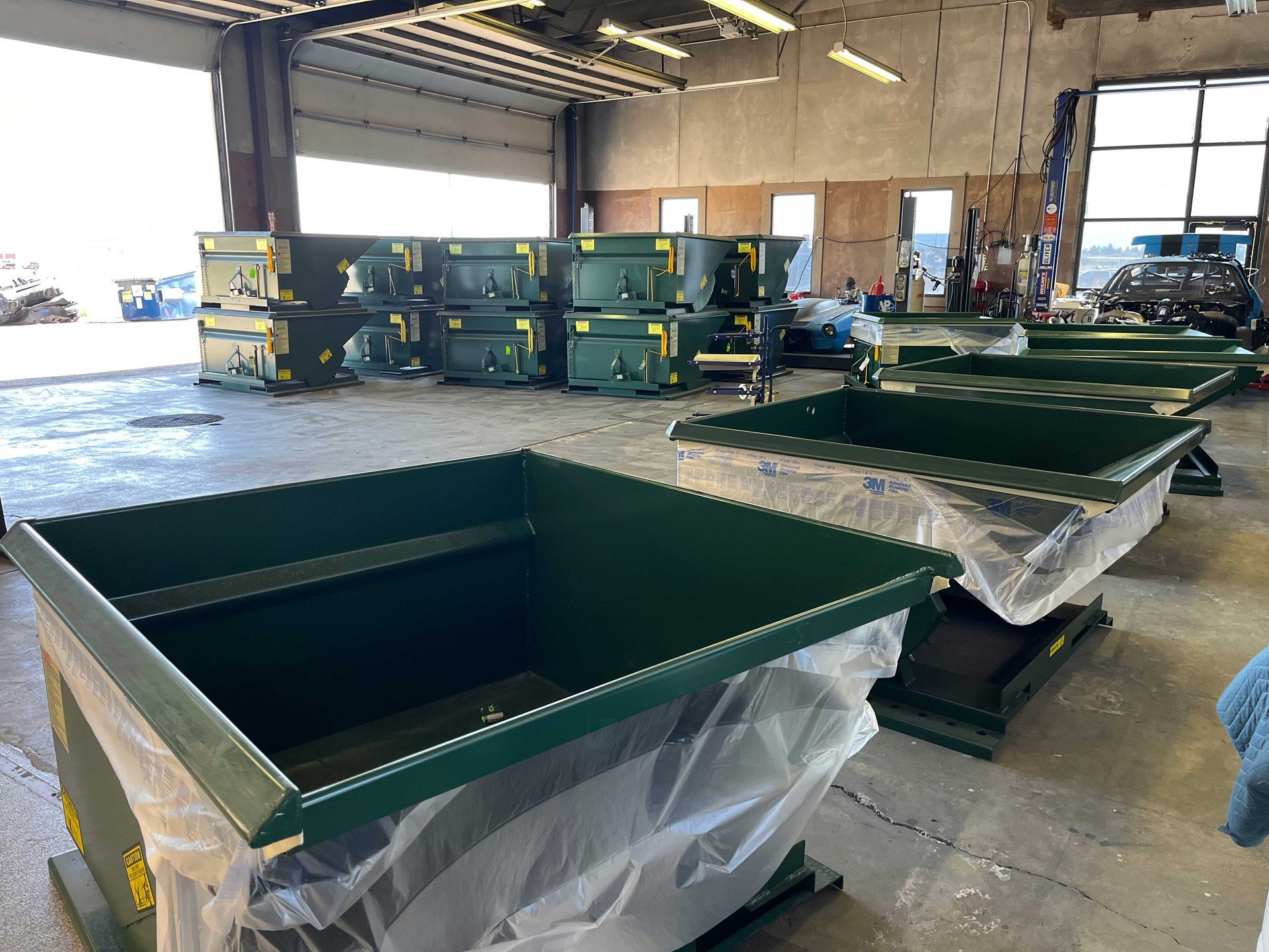 Large, dark green metal containers, some partially wrapped in plastic, sit on the floor of a spacious industrial warehouse.