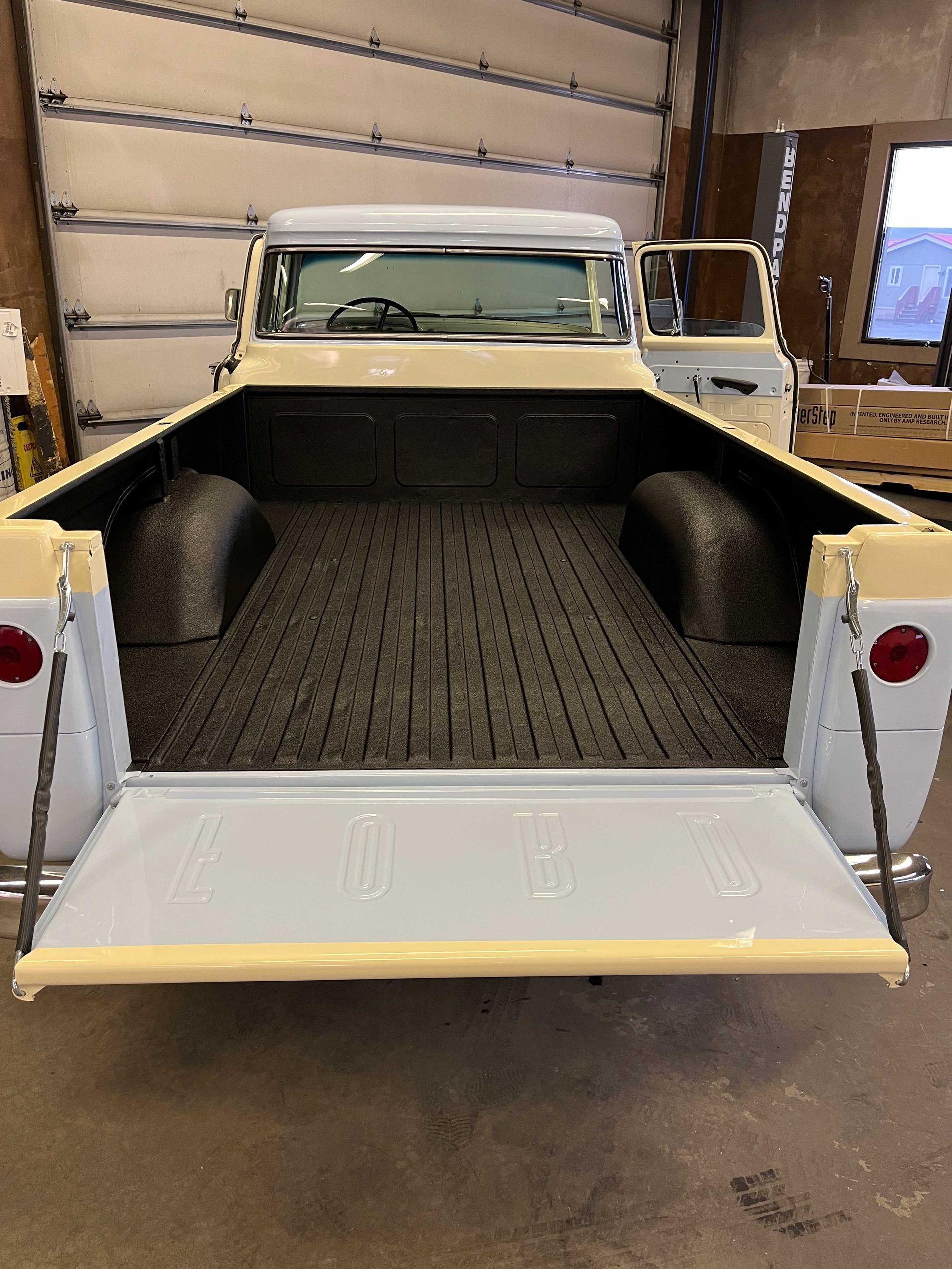 A light blue and cream-colored vintage pickup truck seen from behind with its tailgate down and a textured bed liner.