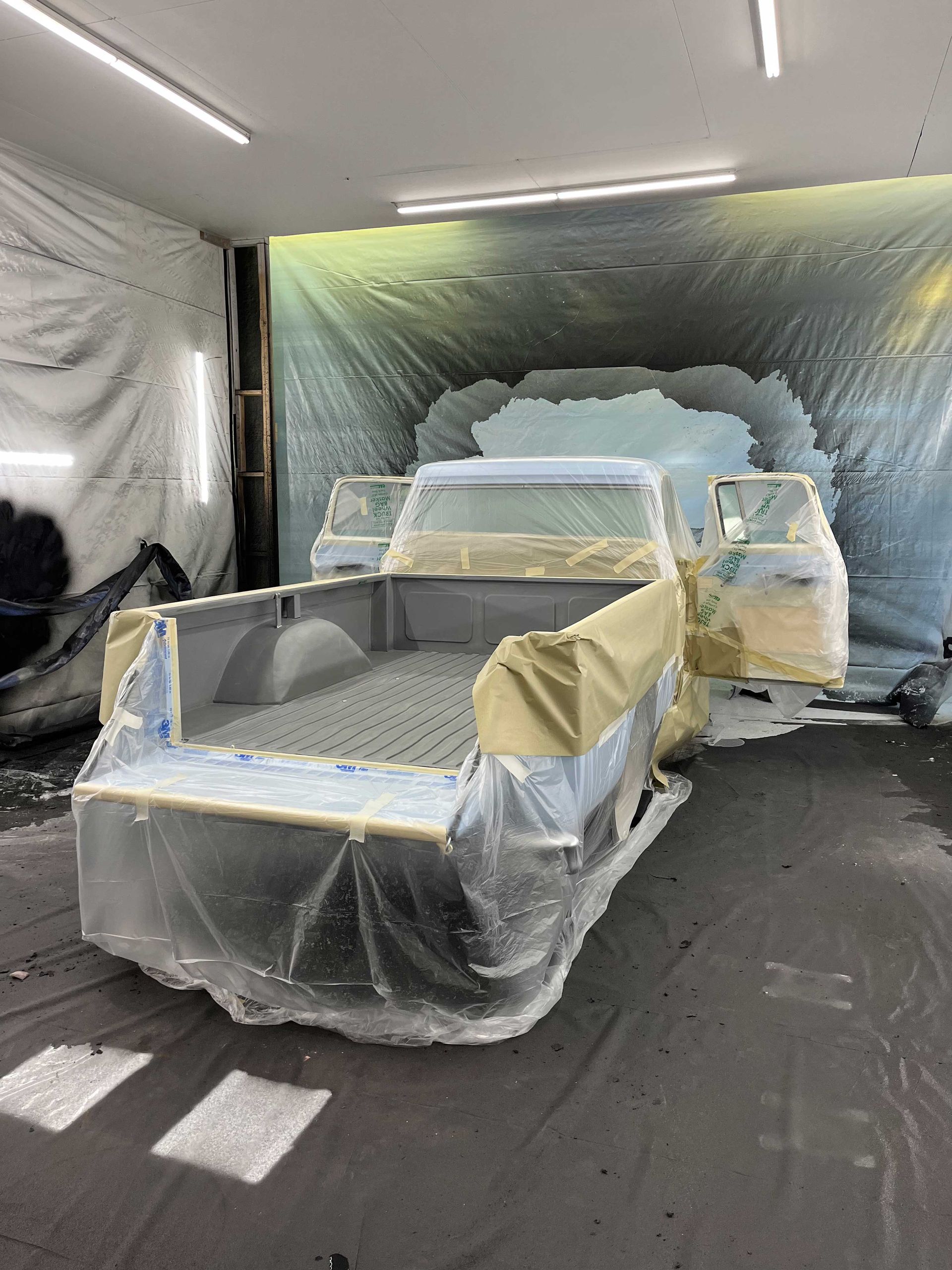 A pickup truck masked with plastic and tape in an auto body paint booth, prepared for painting.