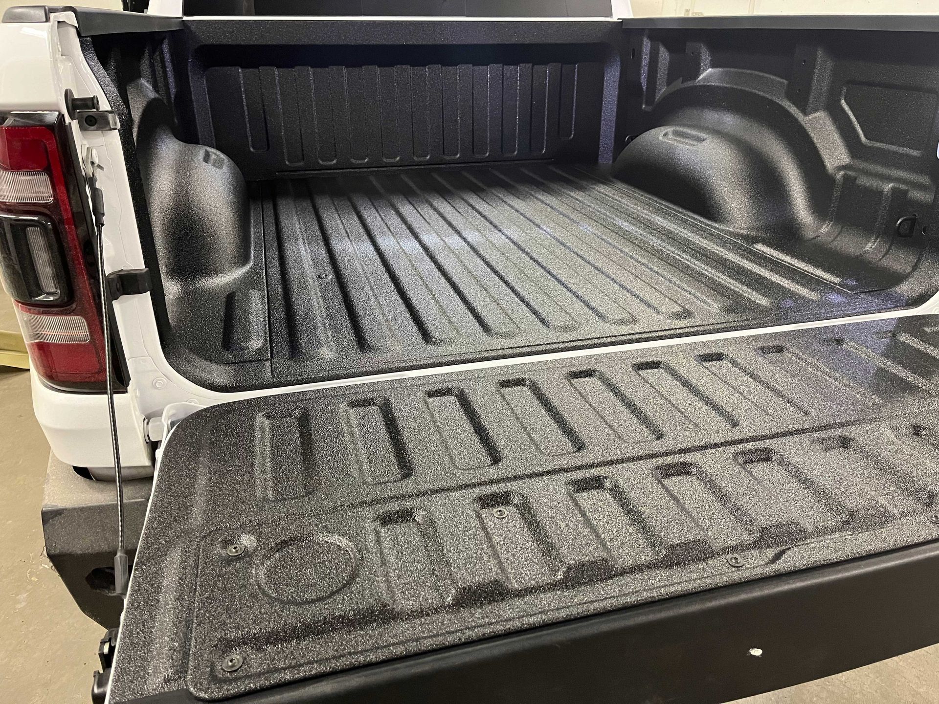 The bed of a white pickup truck coated in a black, textured spray-on liner with the tailgate lowered.