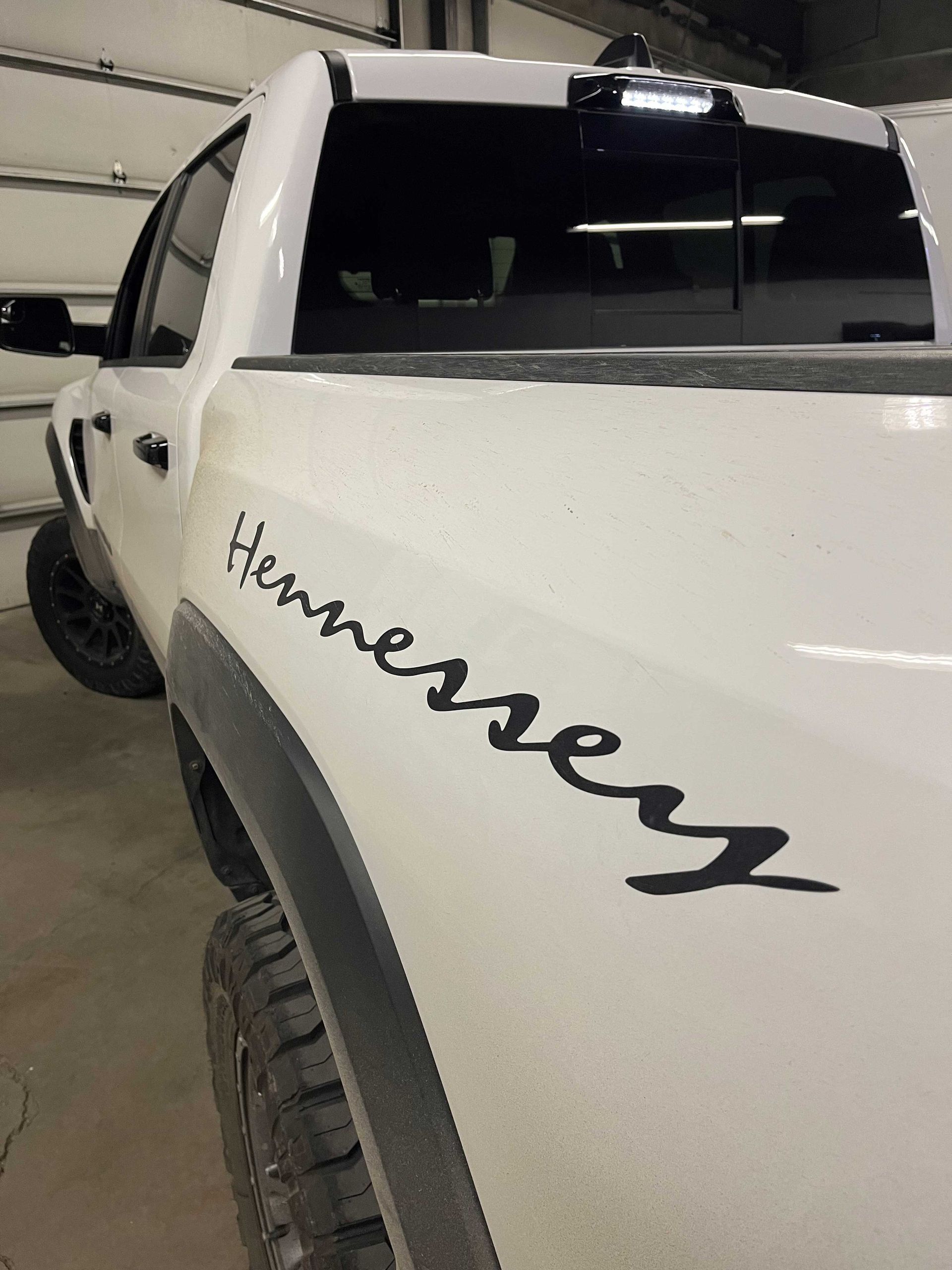 A white pickup truck with a black Hennessey logo decal on the side panel, parked in a garage.