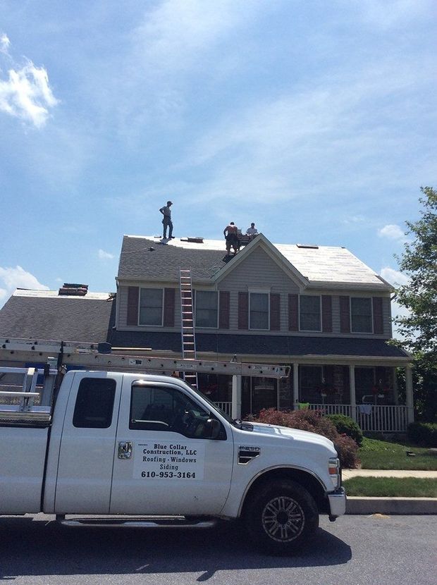 Roofers on a house with a white truck in front. Sunny day.