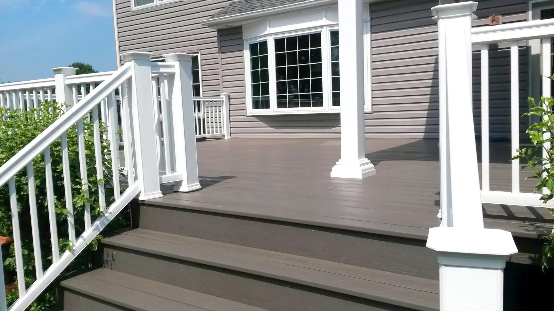 Gray deck with white railing, steps leading up to the house with large window.