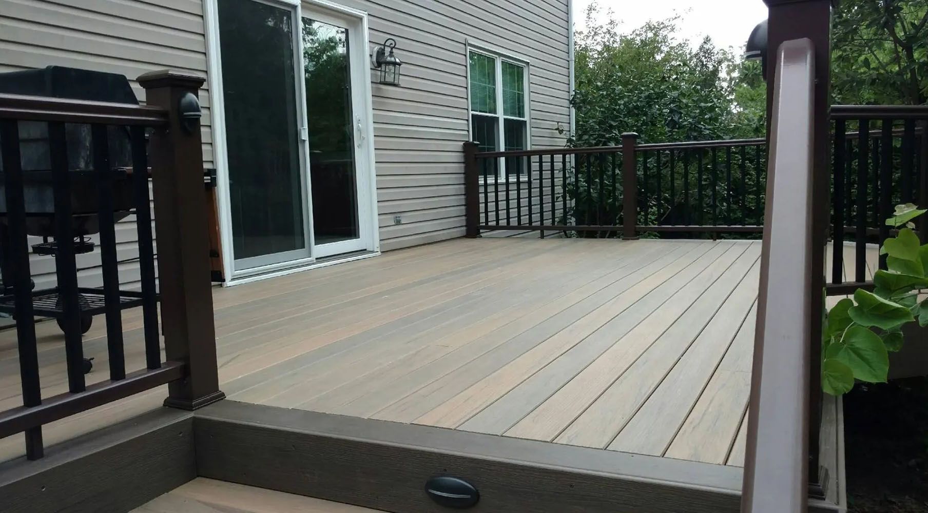 Wooden deck outside a house with sliding glass doors, dark railings, and a small yard.