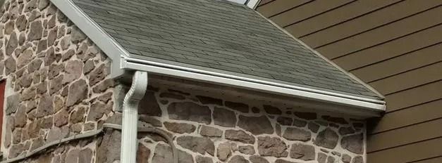 Stone house exterior with a gray roof and white gutters. Brown siding on the right.