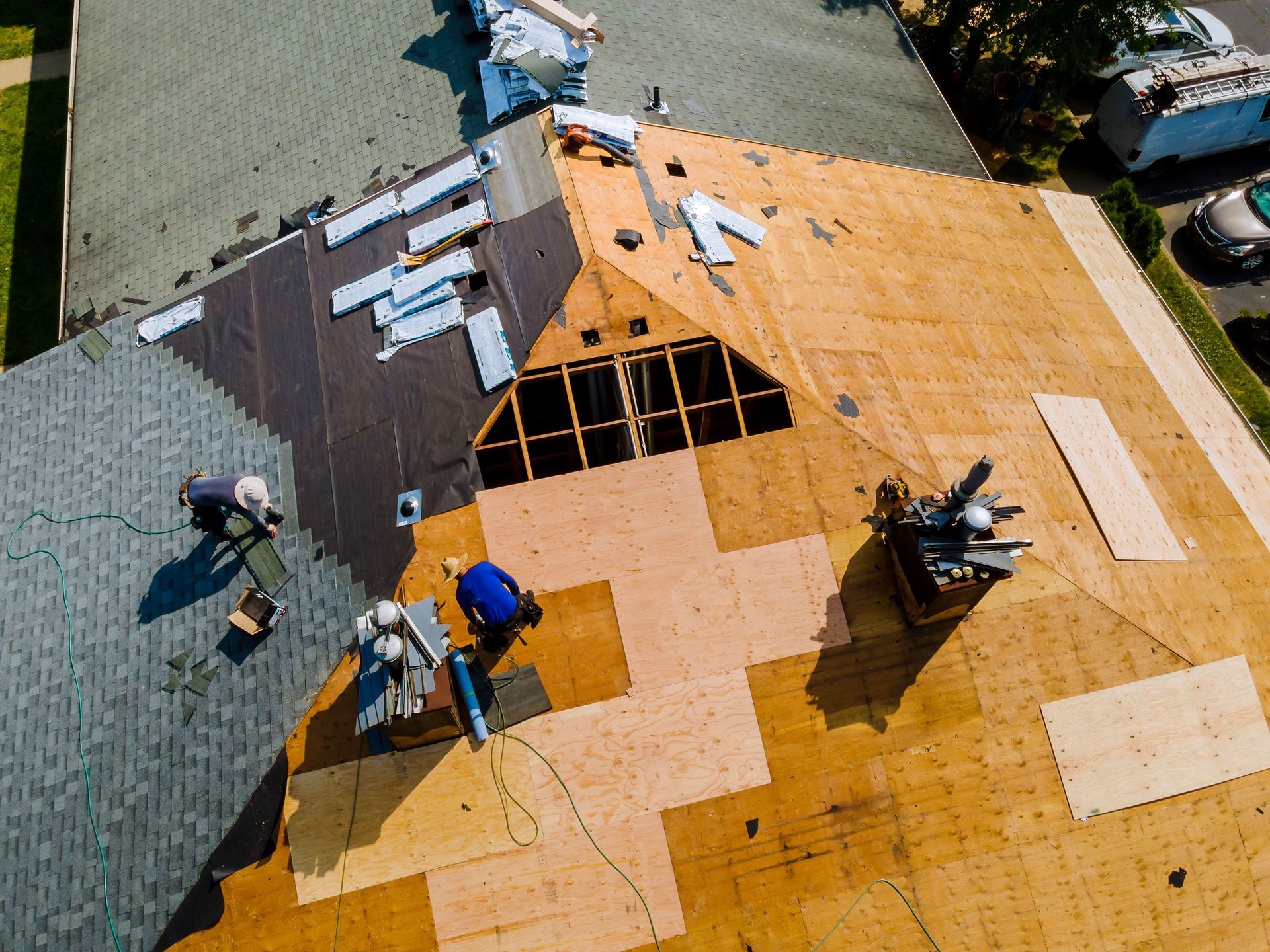 Aerial view of a roof under construction. Workers are installing shingles and repairing the structure.