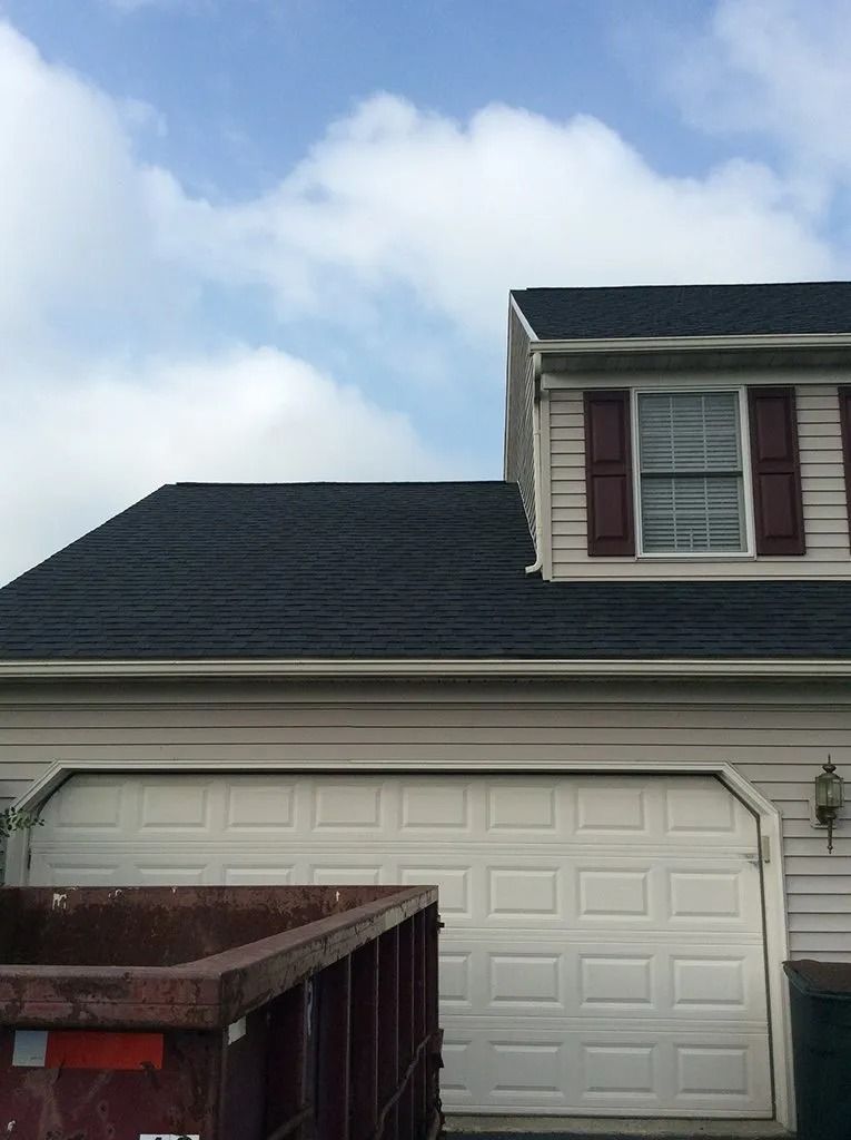 Garage with black roof, white door, and a small upper section with a window and maroon shutters.