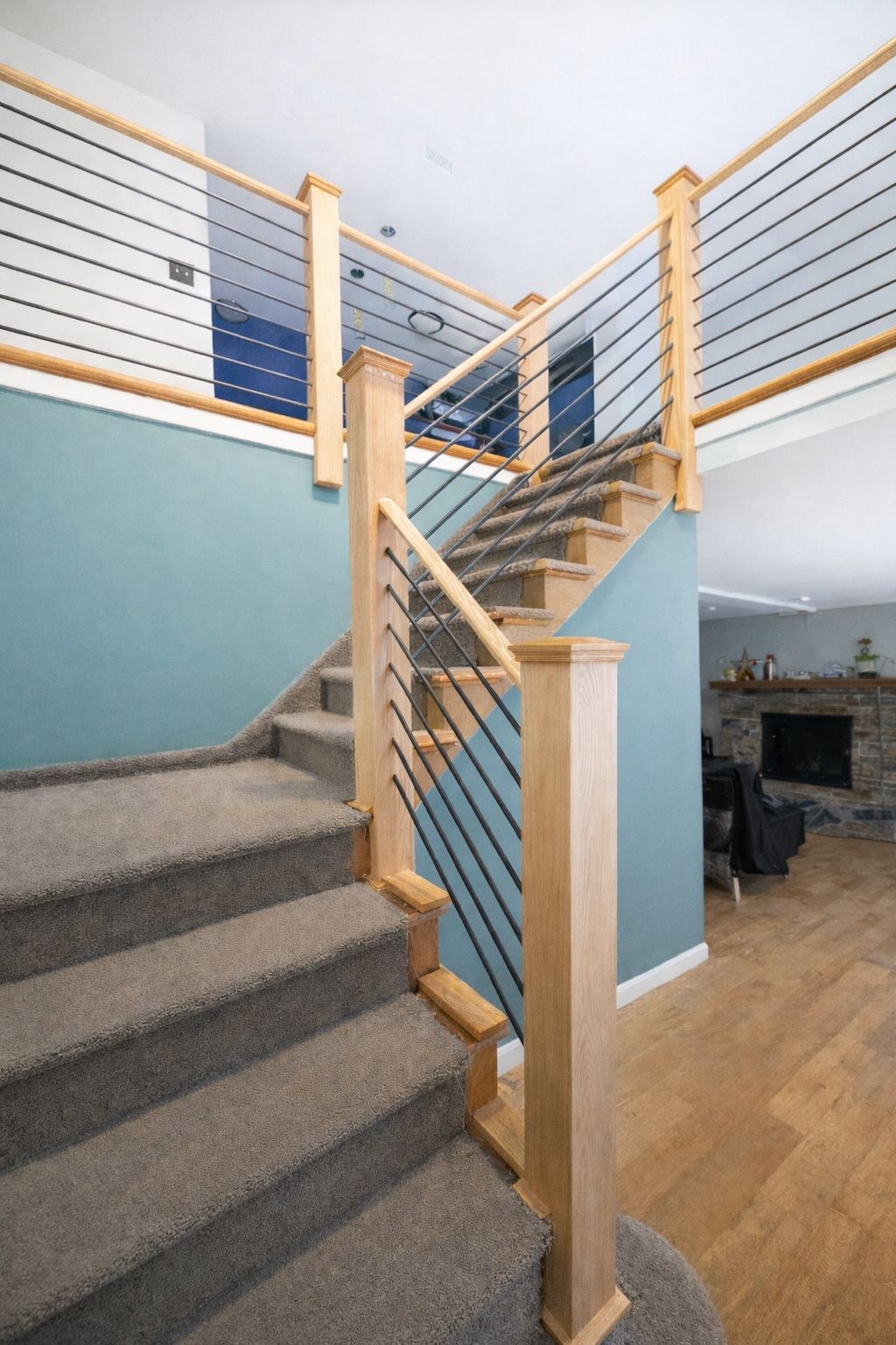 Staircase with wooden posts, metal cable railings, and carpeted steps. Blue and white walls, hardwood floors.