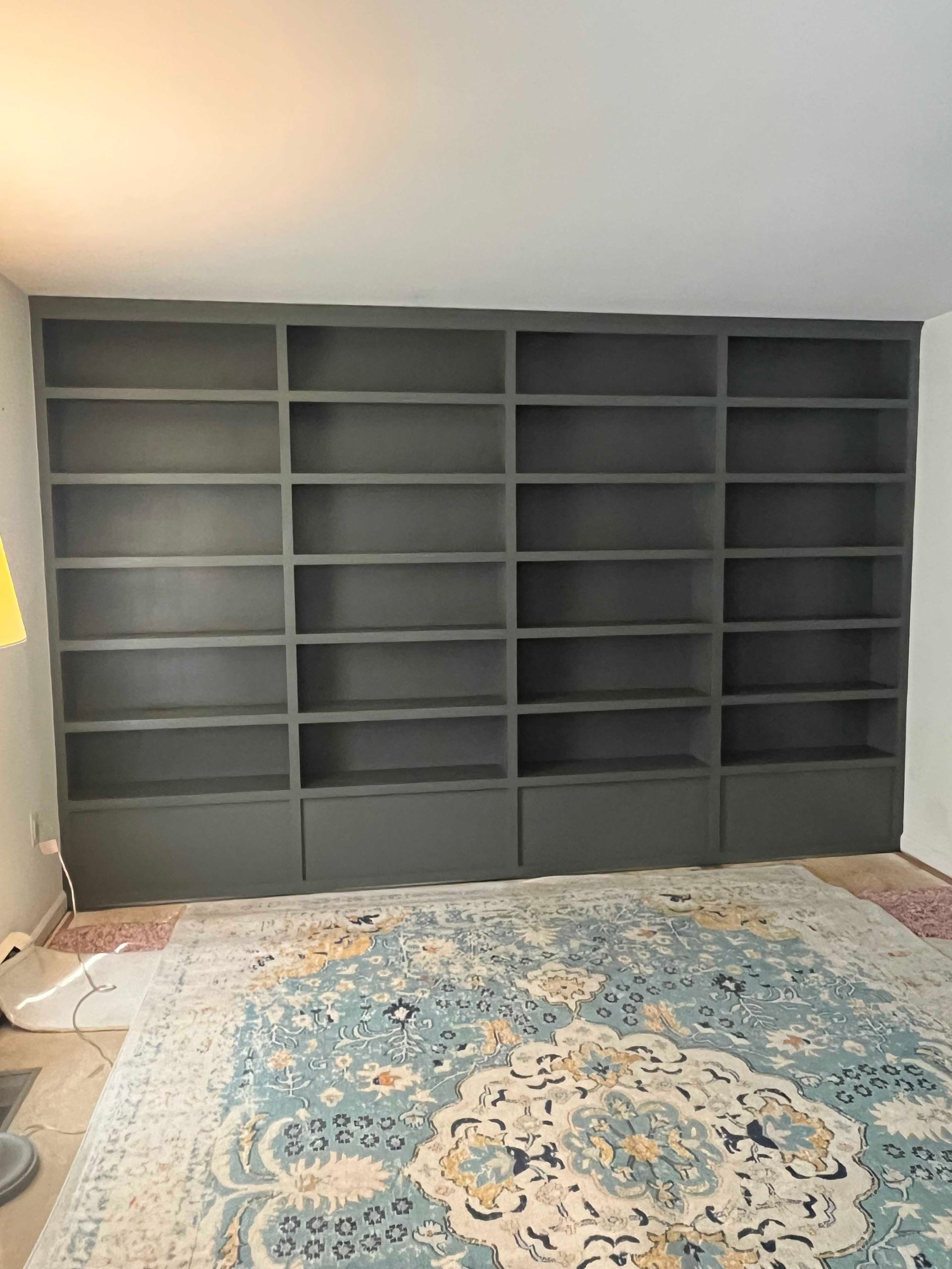 A living room with a rug , shelves , and a lamp.