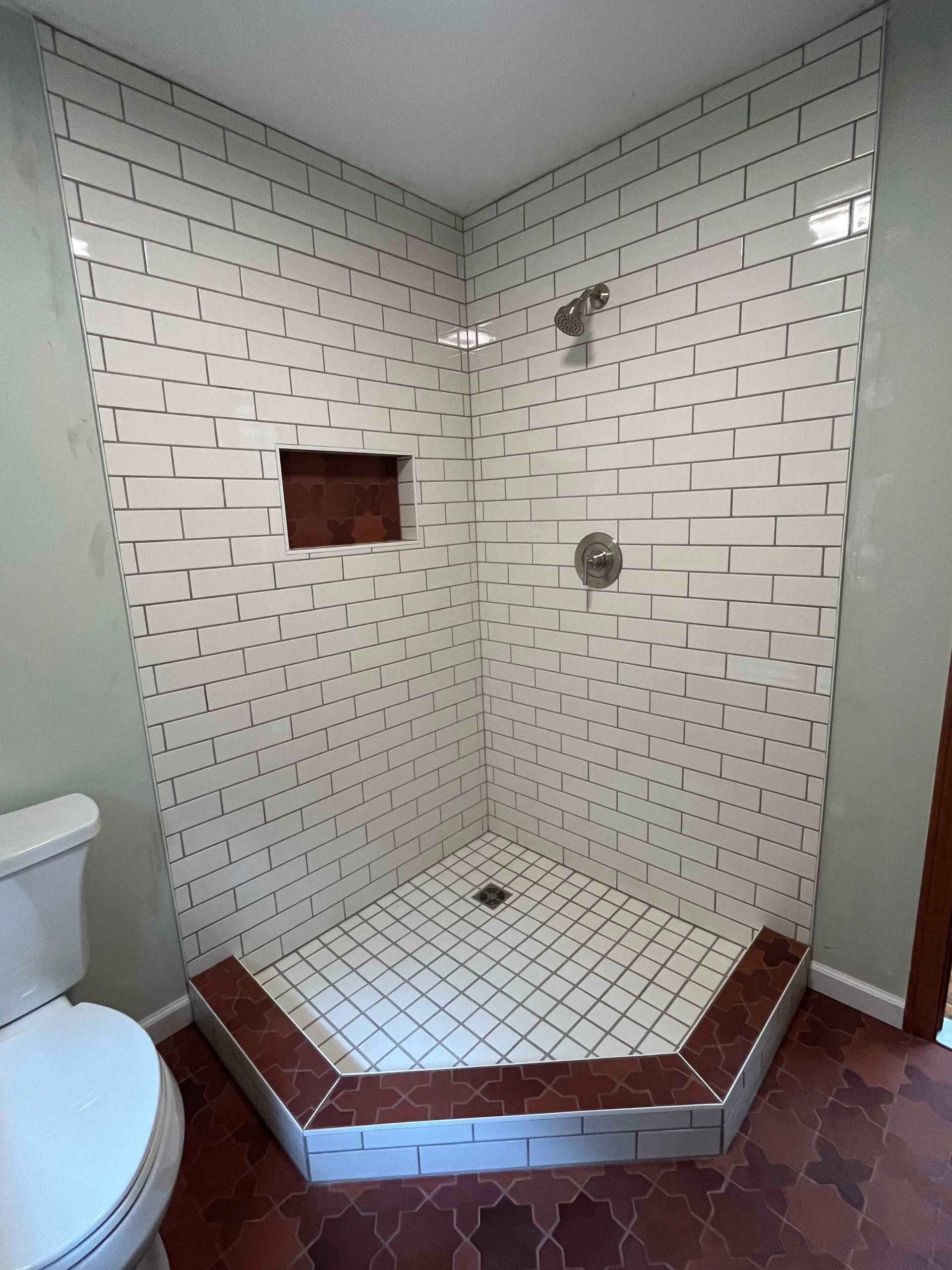 A bathroom with a toilet , shower , and brick wall.