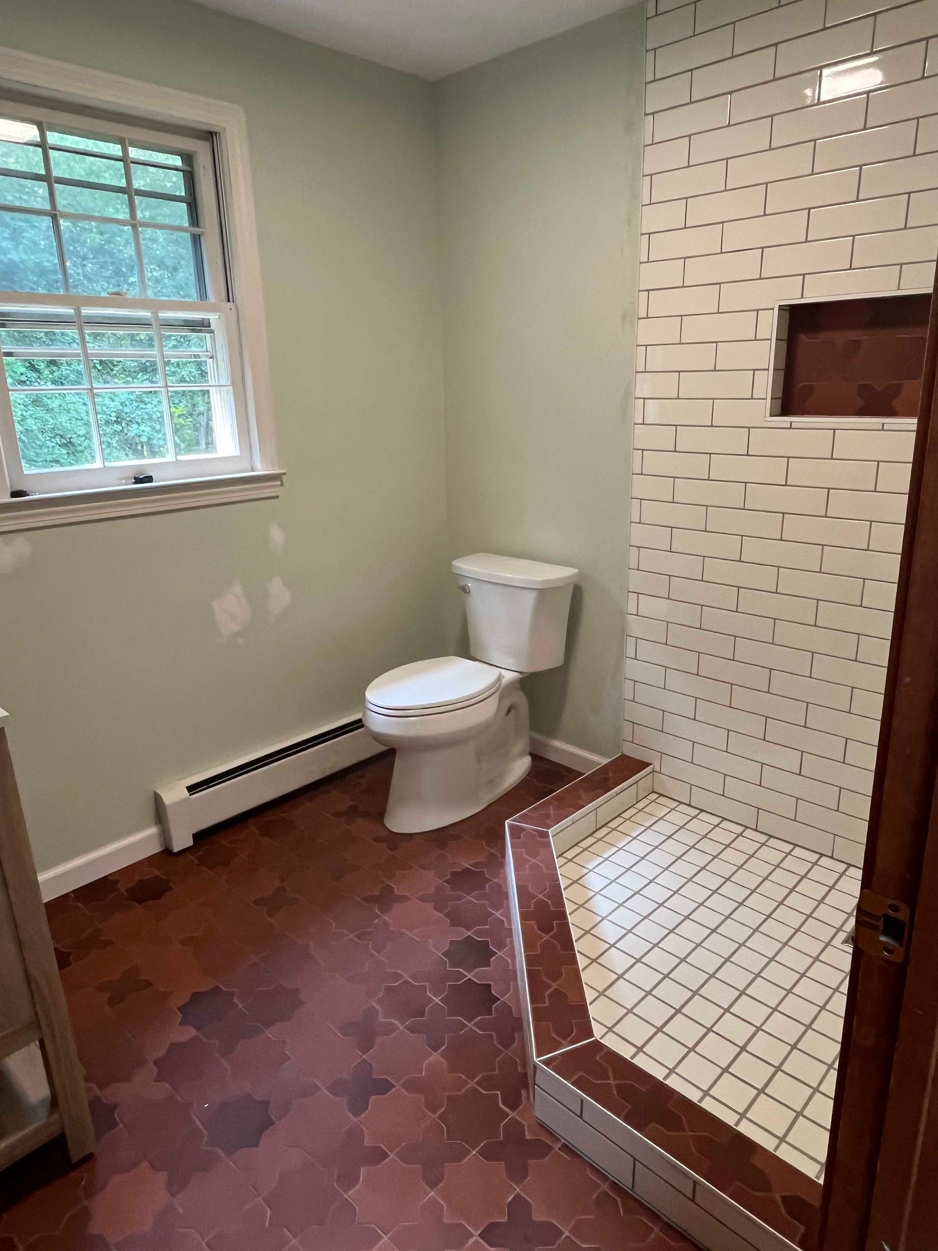 A bathroom with a toilet , shower and window.