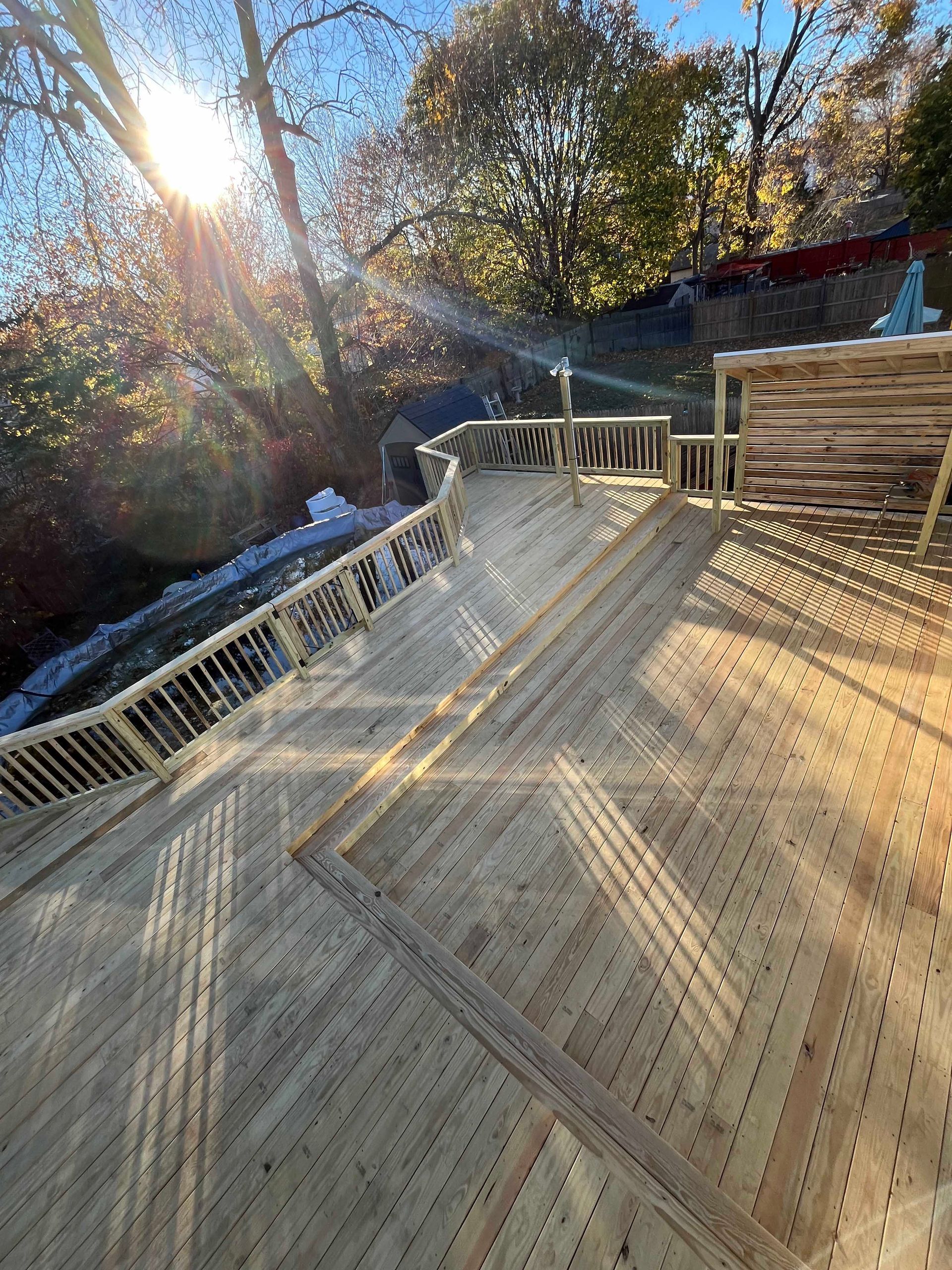 The sun is shining through the trees on a wooden deck.