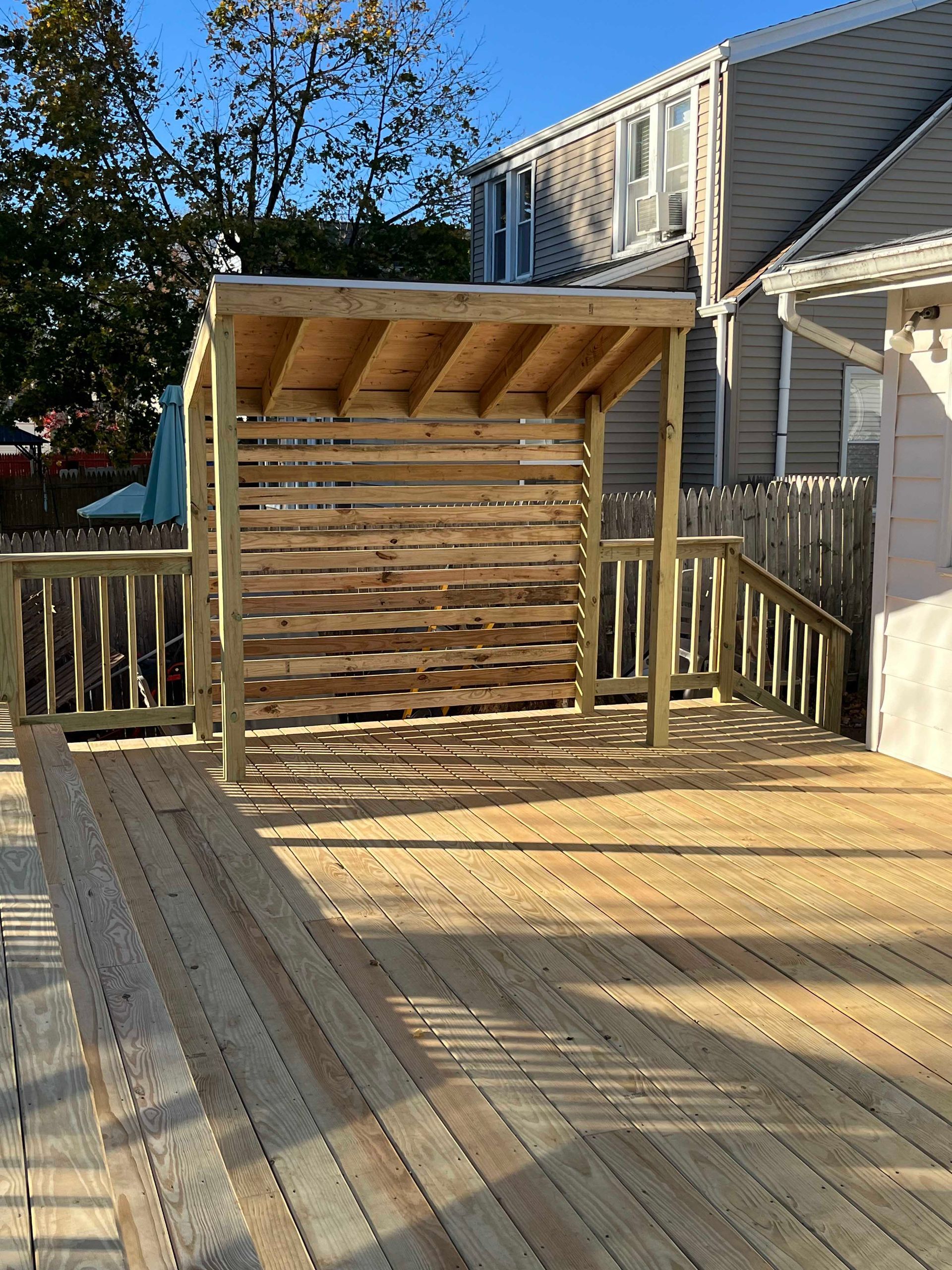 A wooden deck with a pergola on top of it in front of a house.