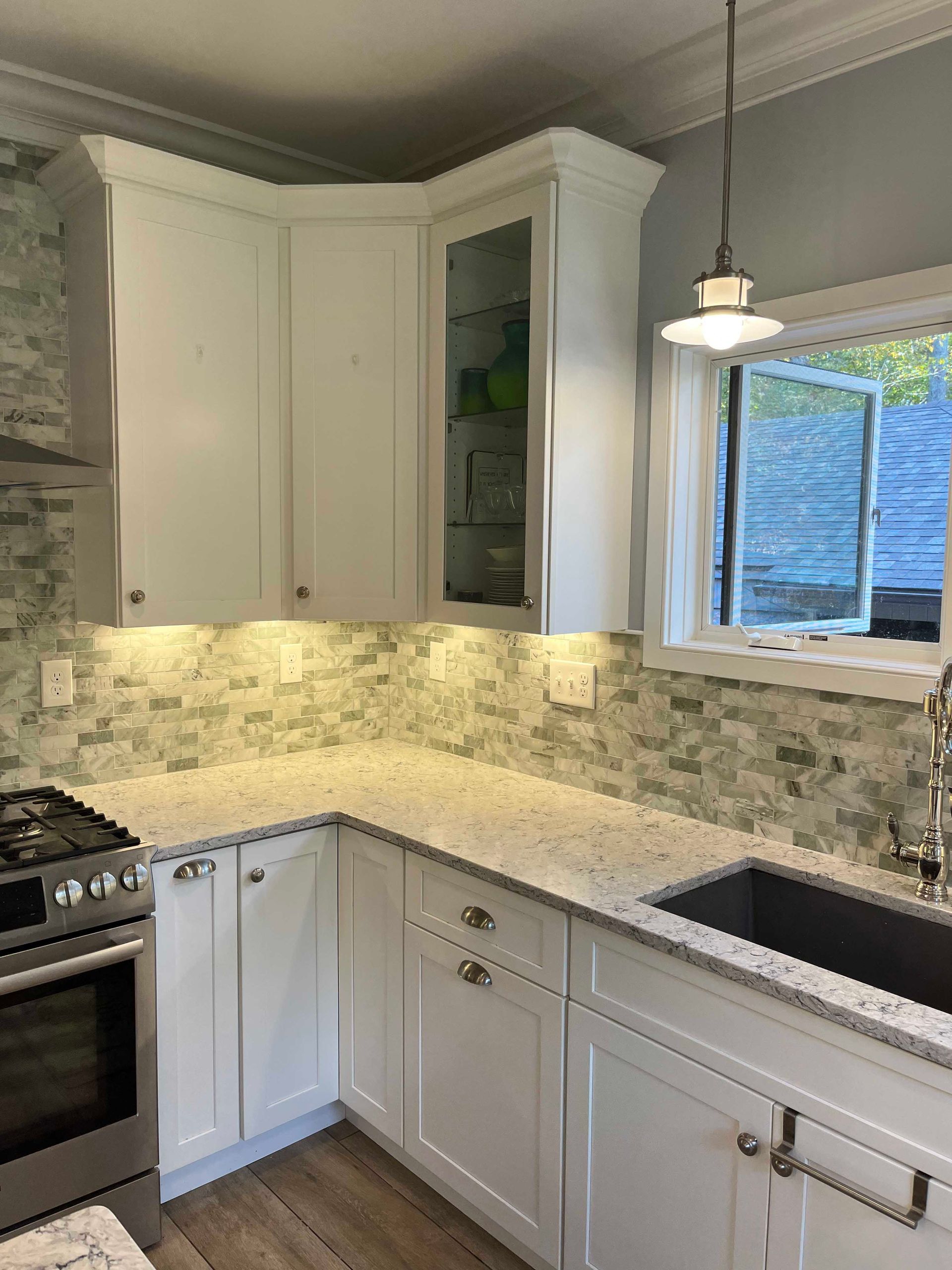 A kitchen with white cabinets , a stove , a sink , and a window.