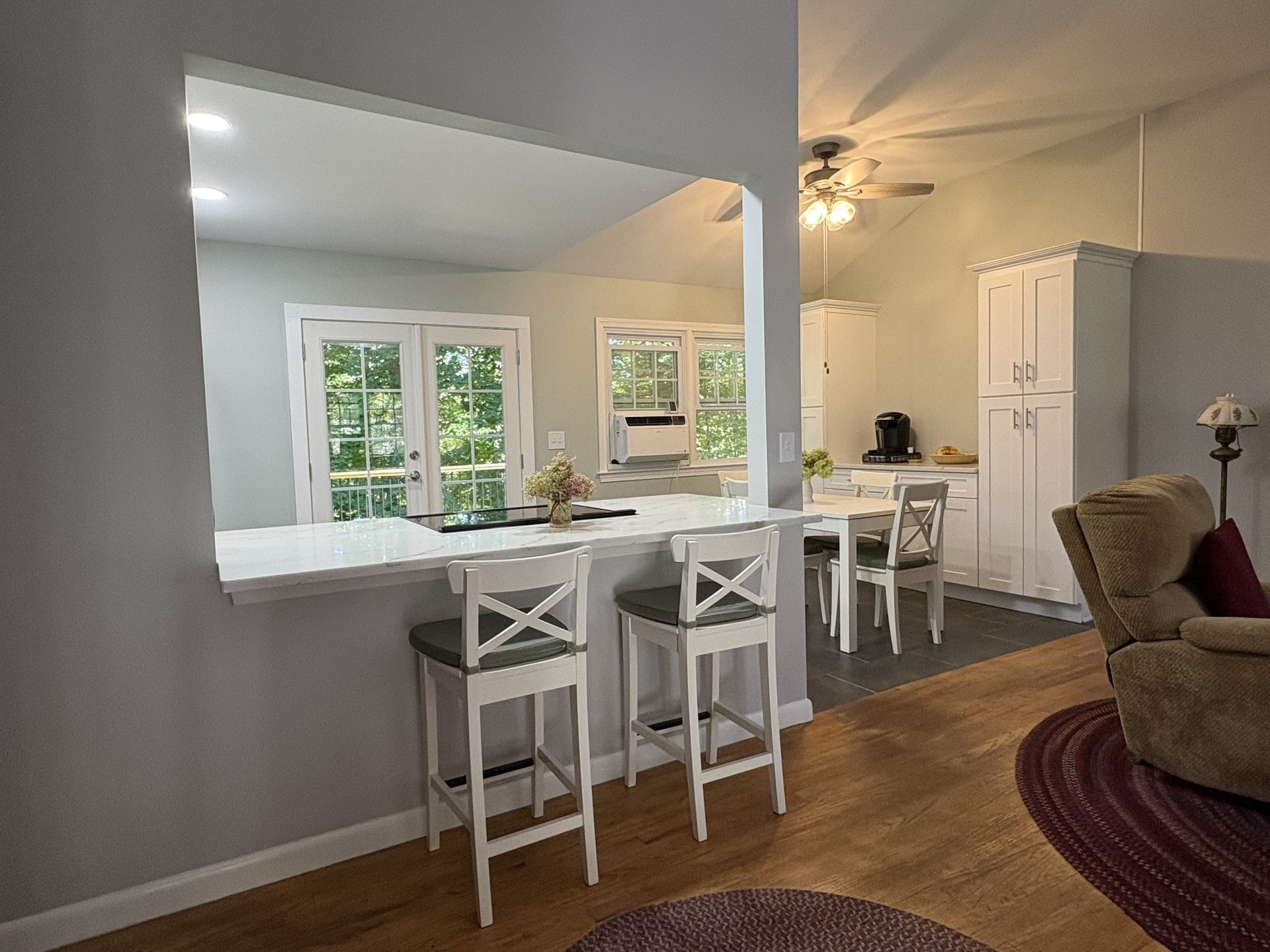 Kitchen with breakfast bar, white counters, and X-back stools. Dining area has white cabinets and table.
