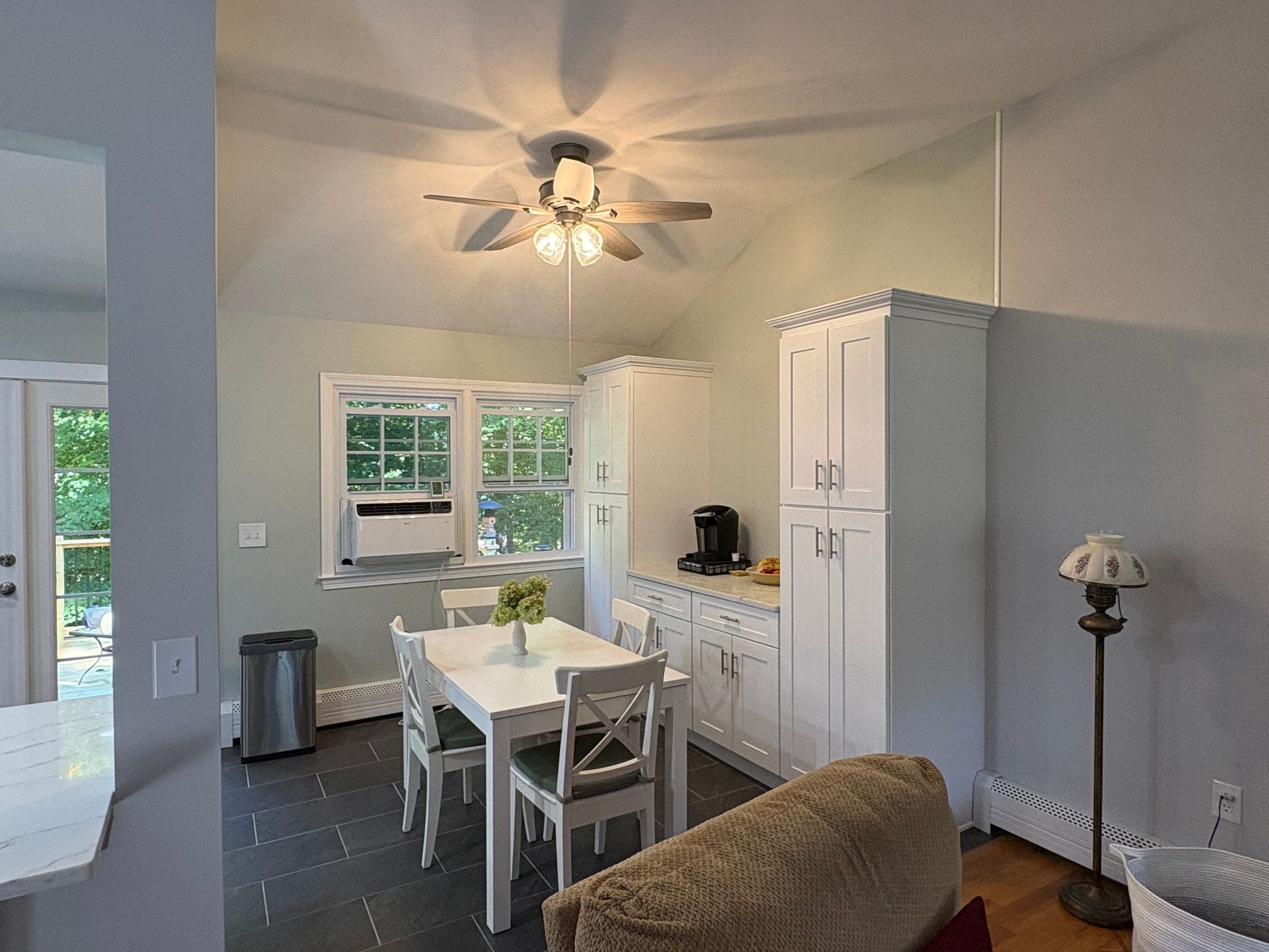 Cozy kitchen with white cabinets, table, and chairs. A window shows greenery outside.
