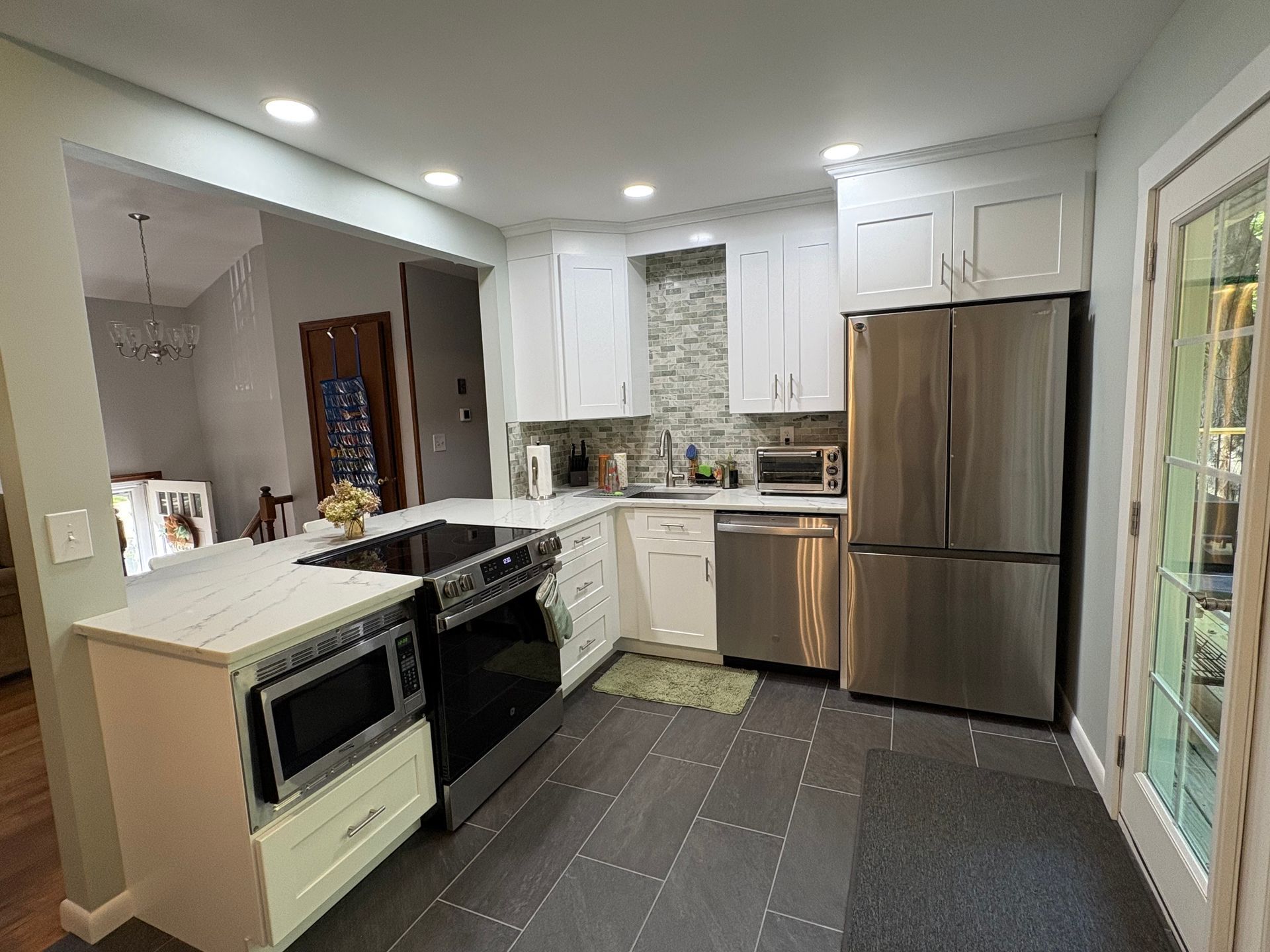 White kitchen with stainless steel appliances, gray floor, and a door to a light-filled area.