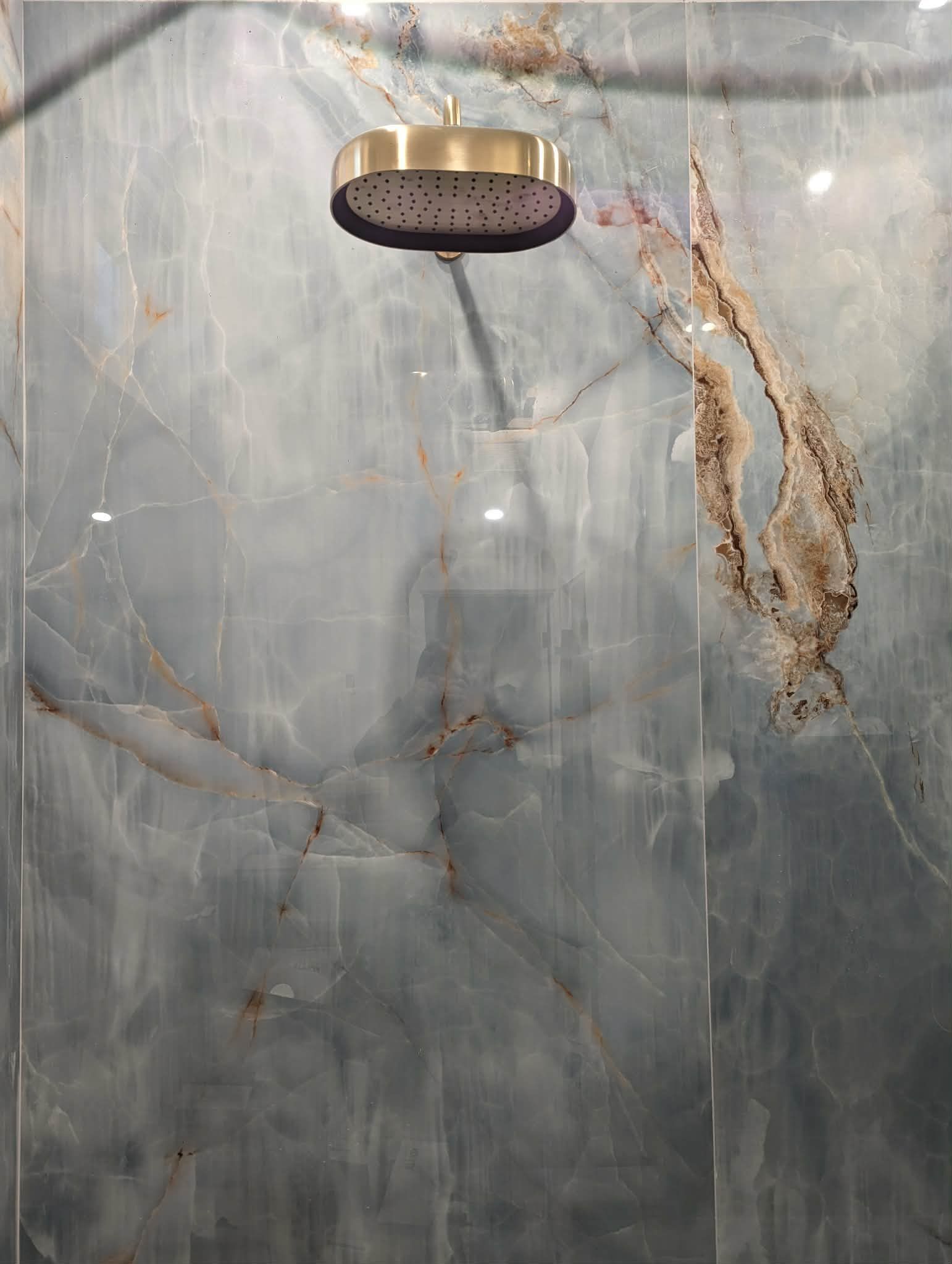 A gray tiled shower wall with a round brass shower head at the top.