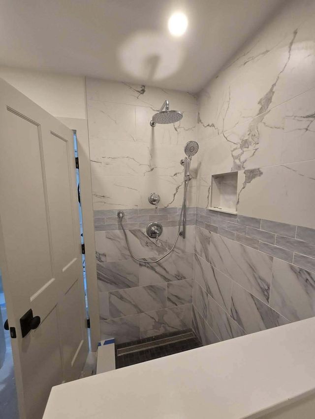 Tiled shower with marble-pattern walls, rainfall showerhead, handheld sprayer, and a built-in shelf.