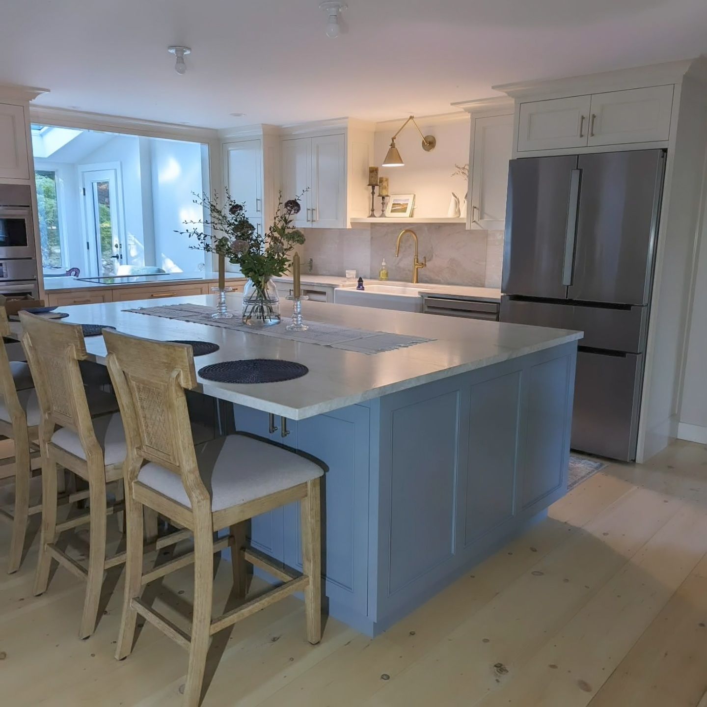 Bright modern kitchen with a large island, wooden stools, and stainless steel refrigerator