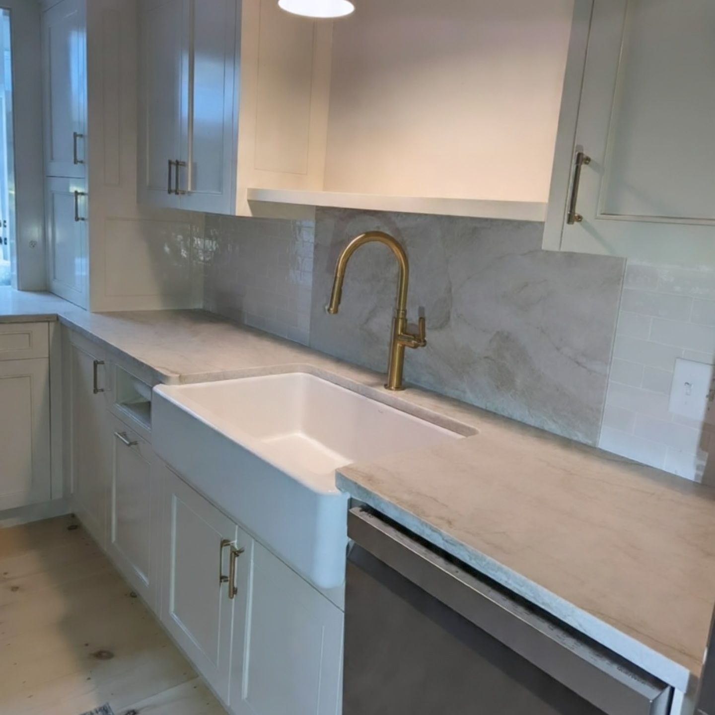 Bright white kitchen with farmhouse sink, gold faucet, marble backsplash, and light countertops