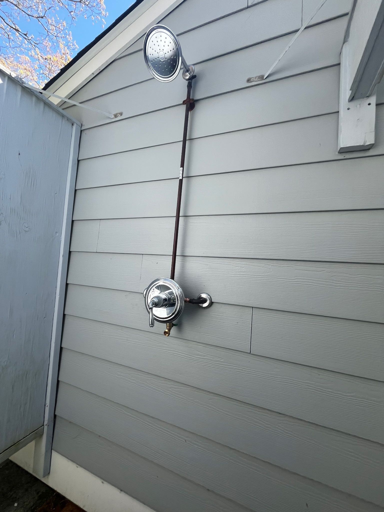Outdoor wall with two chrome shower heads connected by exposed piping on gray siding