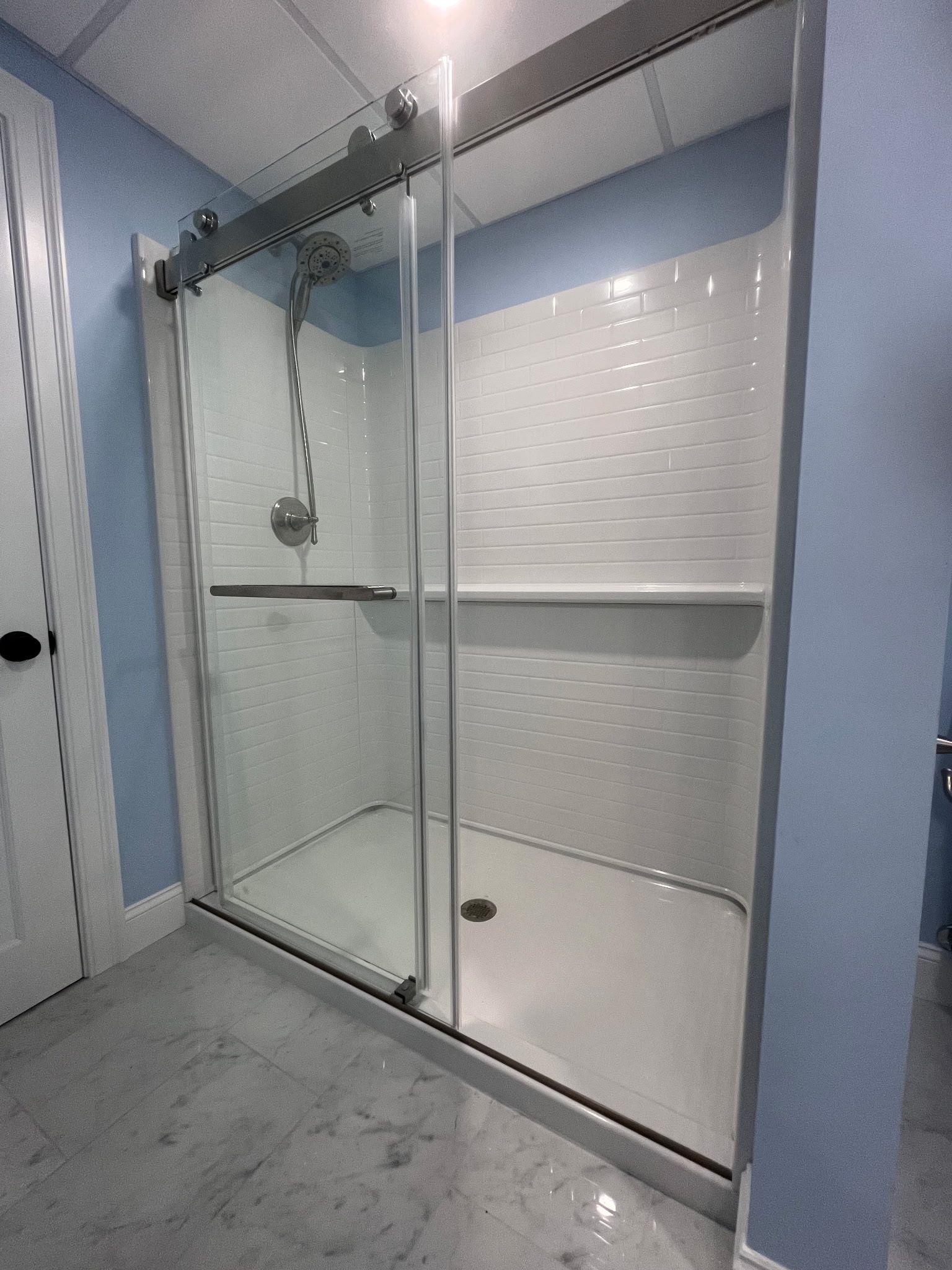 Glass walk-in shower with sliding door, white tiled walls, and blue bathroom walls