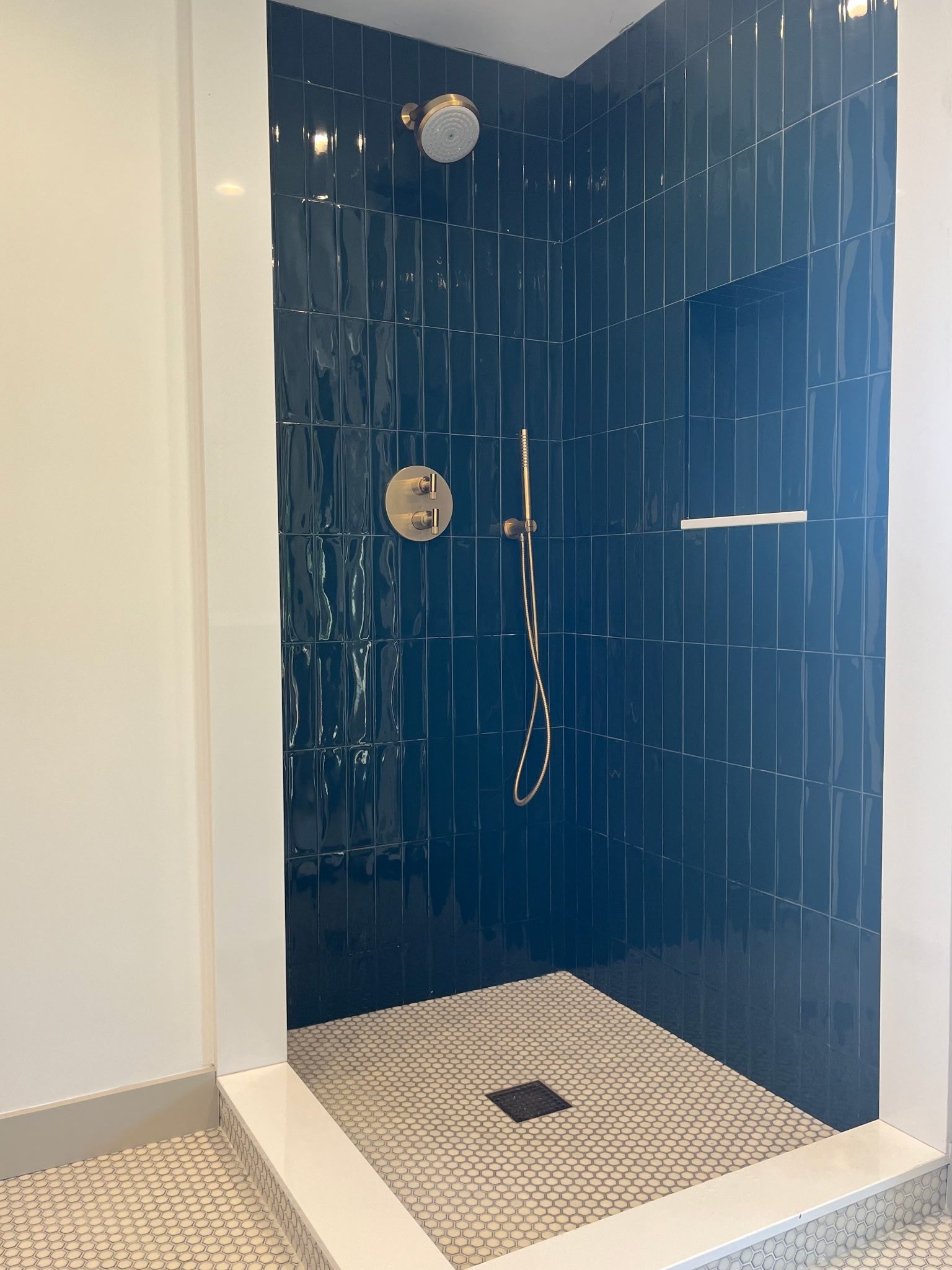Walk-in shower with dark blue tile walls, beige mosaic floor, and chrome shower fixtures