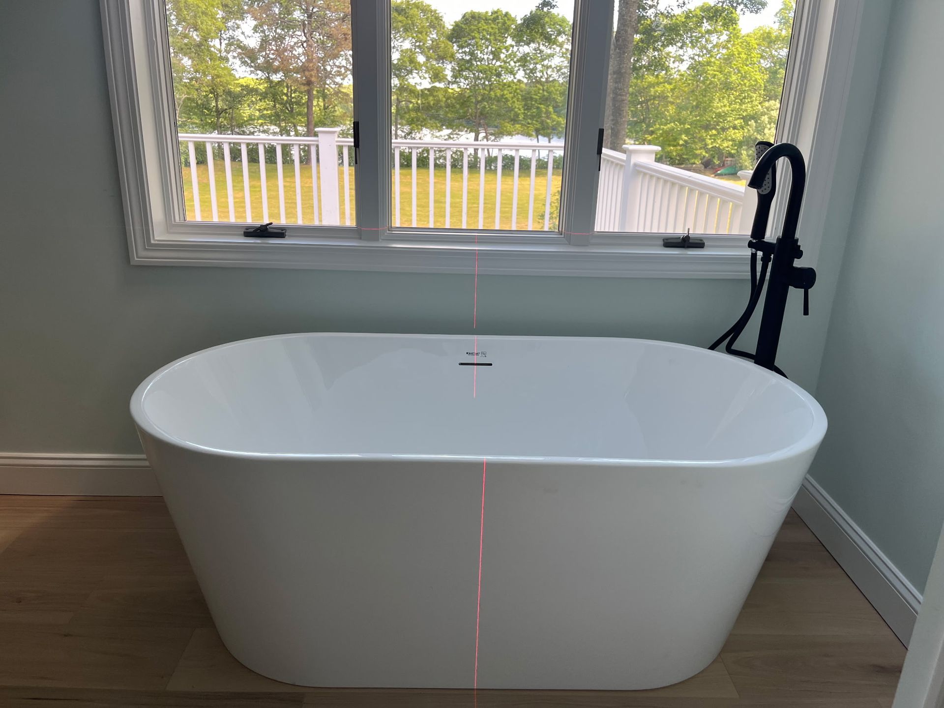White freestanding bathtub by a window overlooking a deck and greenery