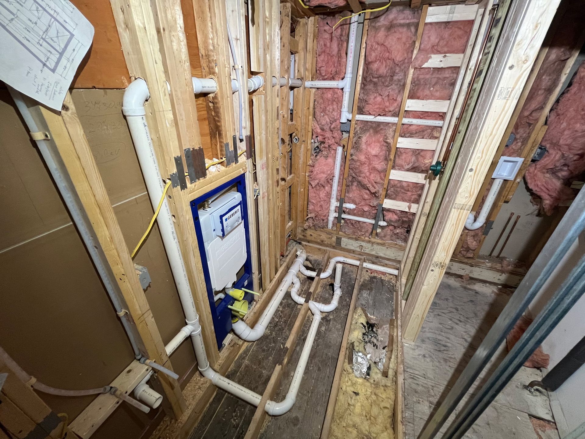 Exposed wall studs and plumbing in an unfinished bathroom with a toilet and shower valve rough-in.