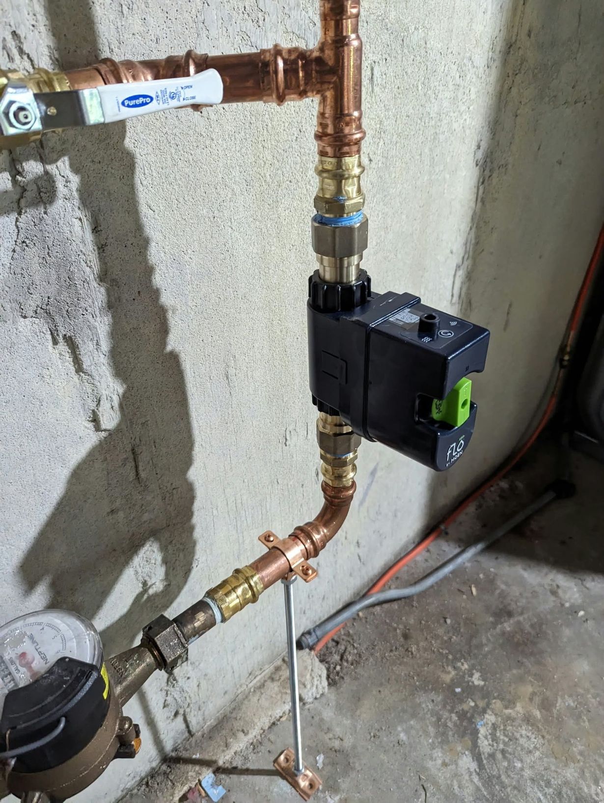 Copper plumbing pipes with a black valve/actuator mounted on a wall near the floor